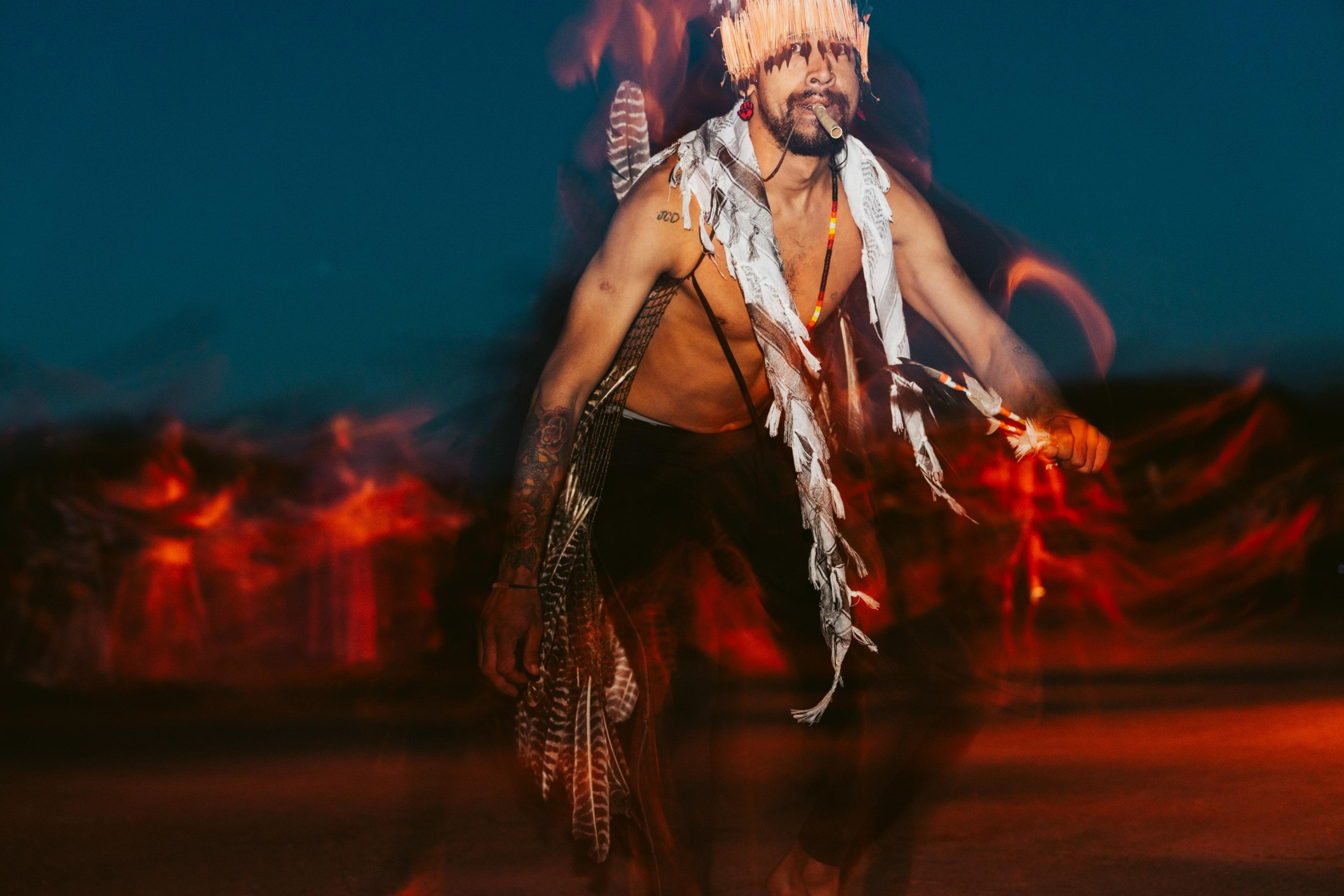 A close up photo of a person dressed in traditional indigenous clothing performing in twilight hours