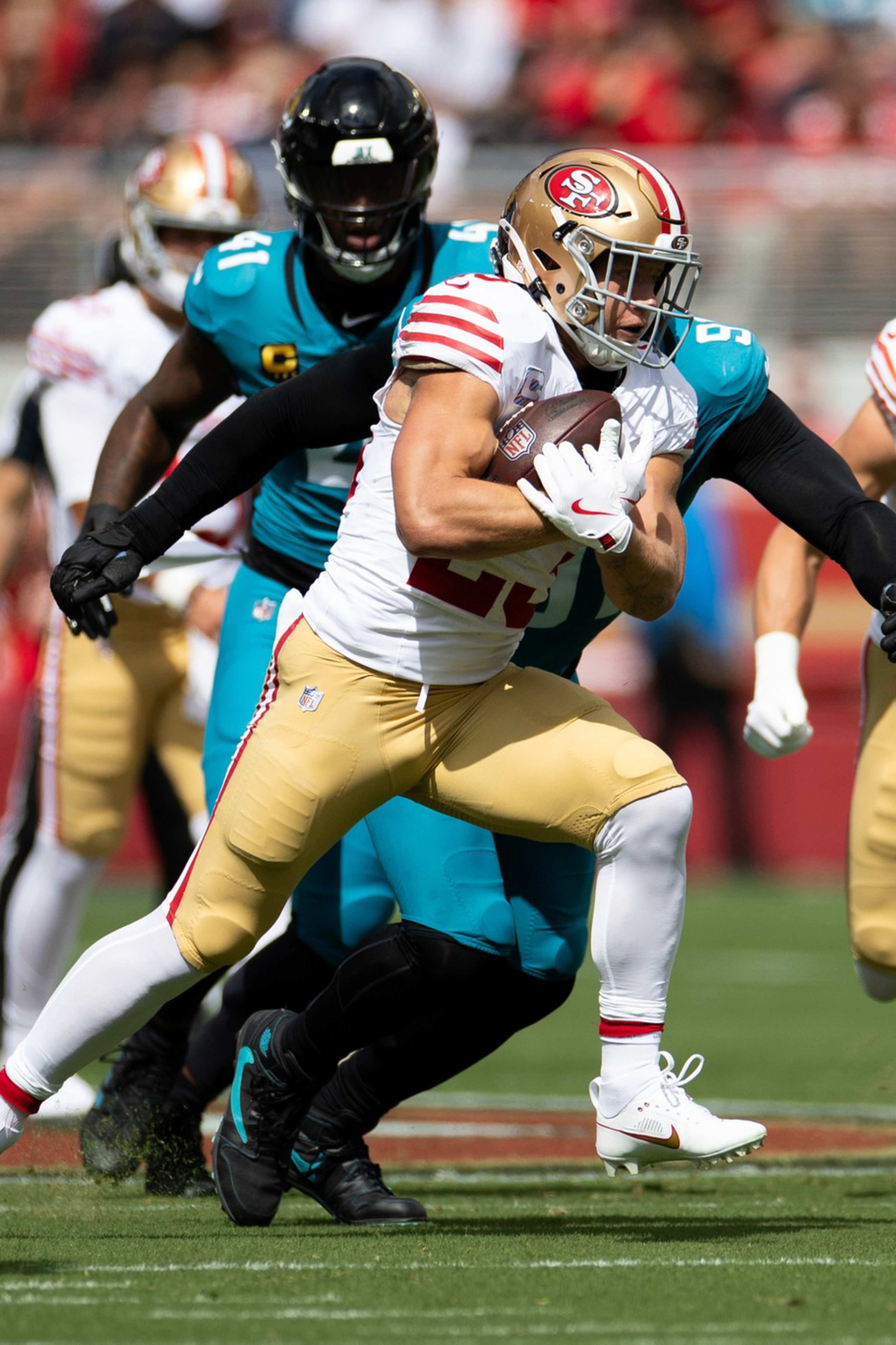 A San Francisco 49ers player runs with the football while being chased and tackled by players from the Jacksonville Jaguars during a game.