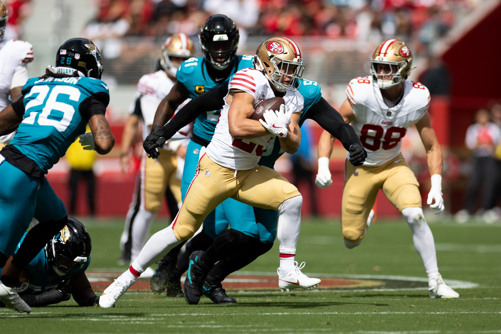 A San Francisco 49ers player runs with the football while being chased and tackled by players from the Jacksonville Jaguars during a game.