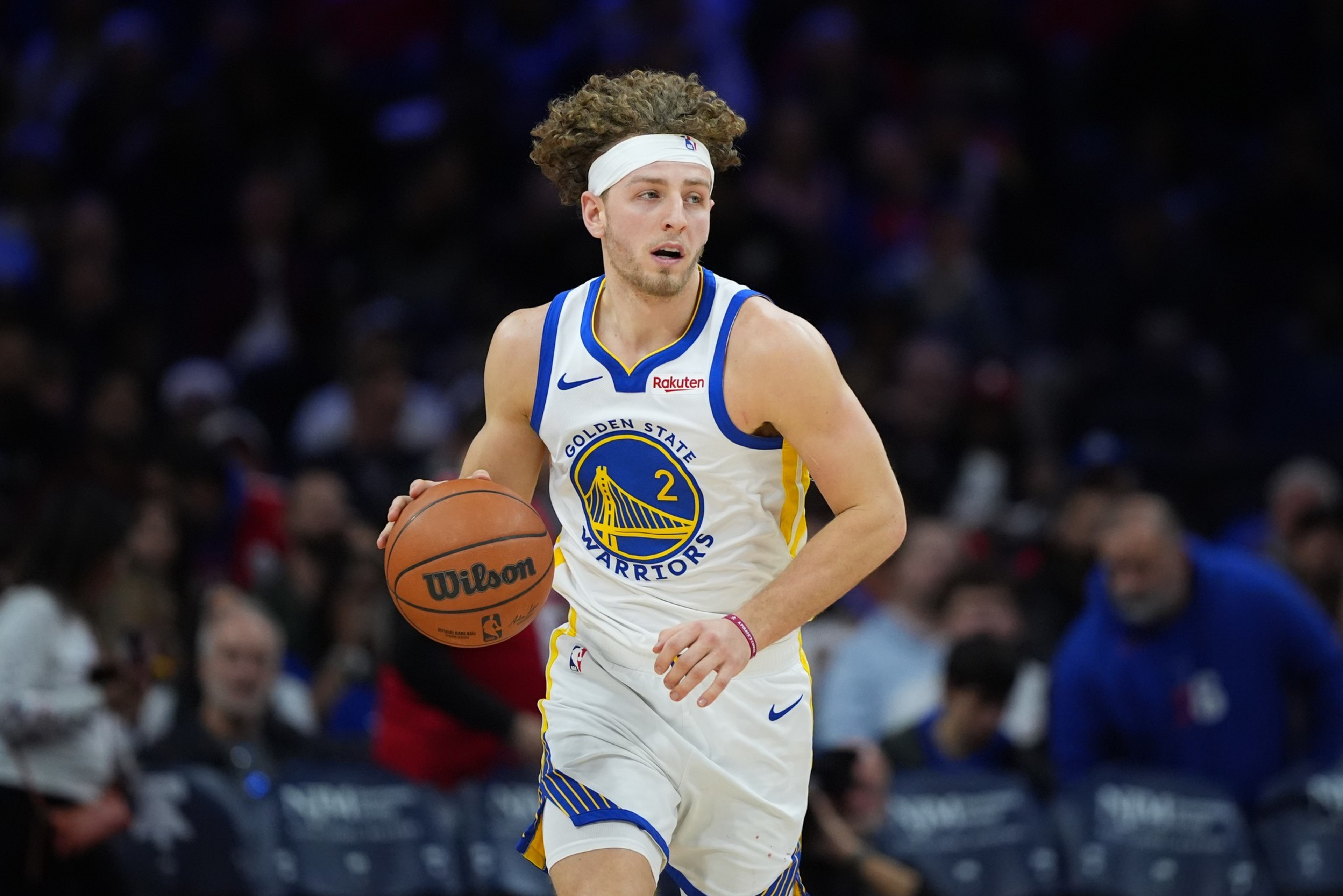 A basketball player wearing a Golden State Warriors uniform with number 2 dribbles a Wilson basketball on the court.