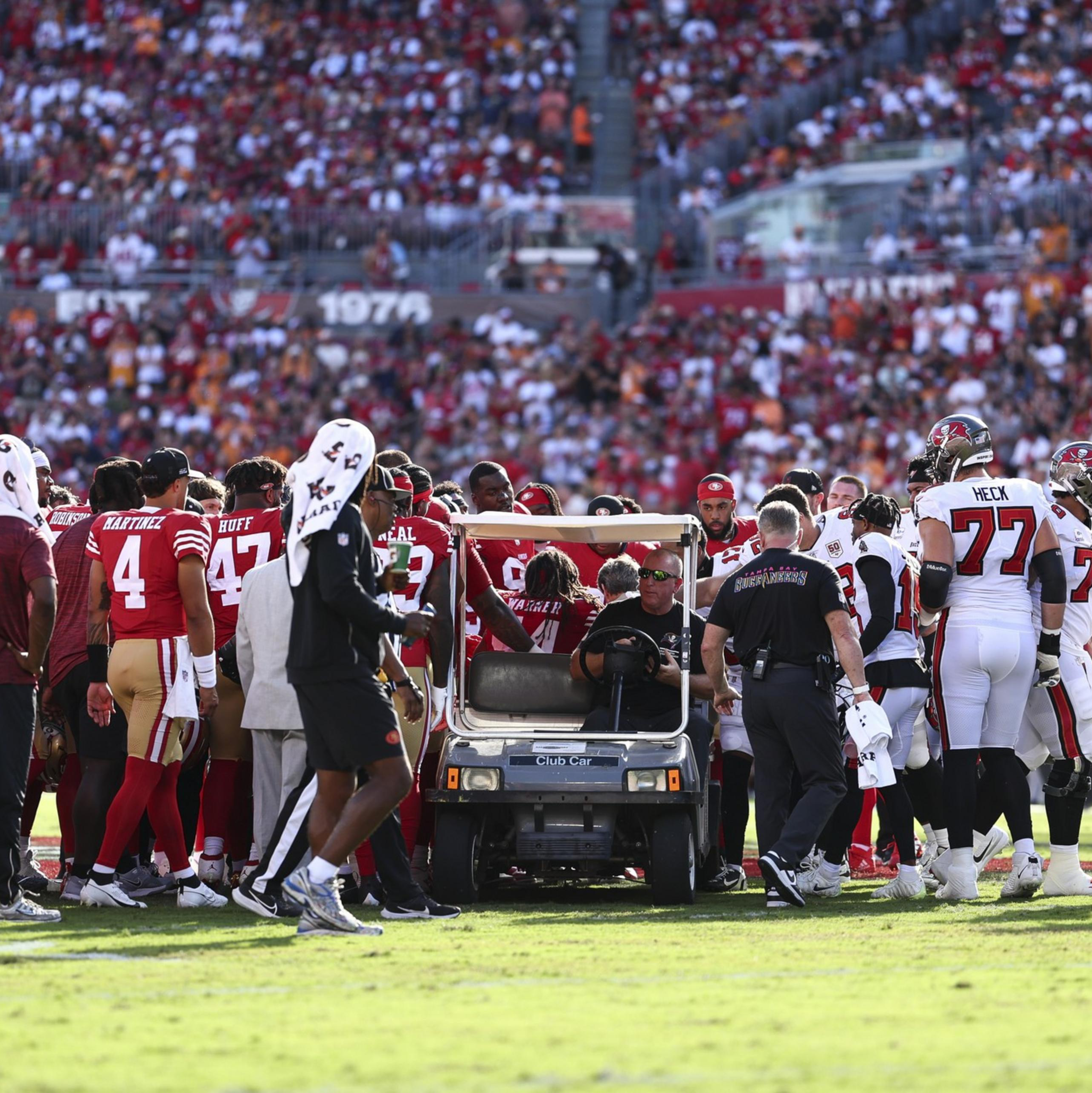A football player is being taken off the field on a medical cart surrounded by coaches, teammates, and referees during a crowded game.