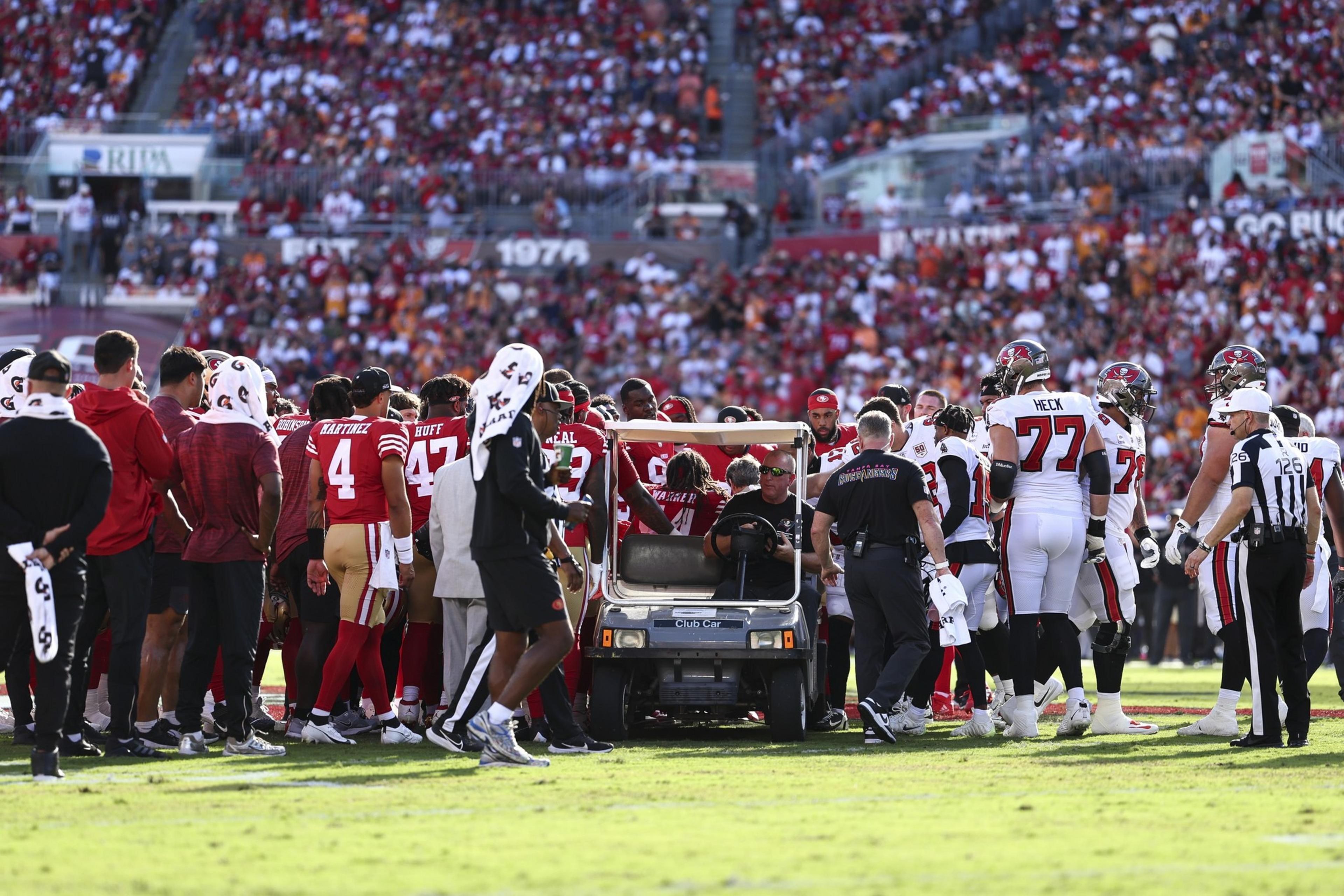 A football player is being taken off the field on a medical cart surrounded by coaches, teammates, and referees during a crowded game.