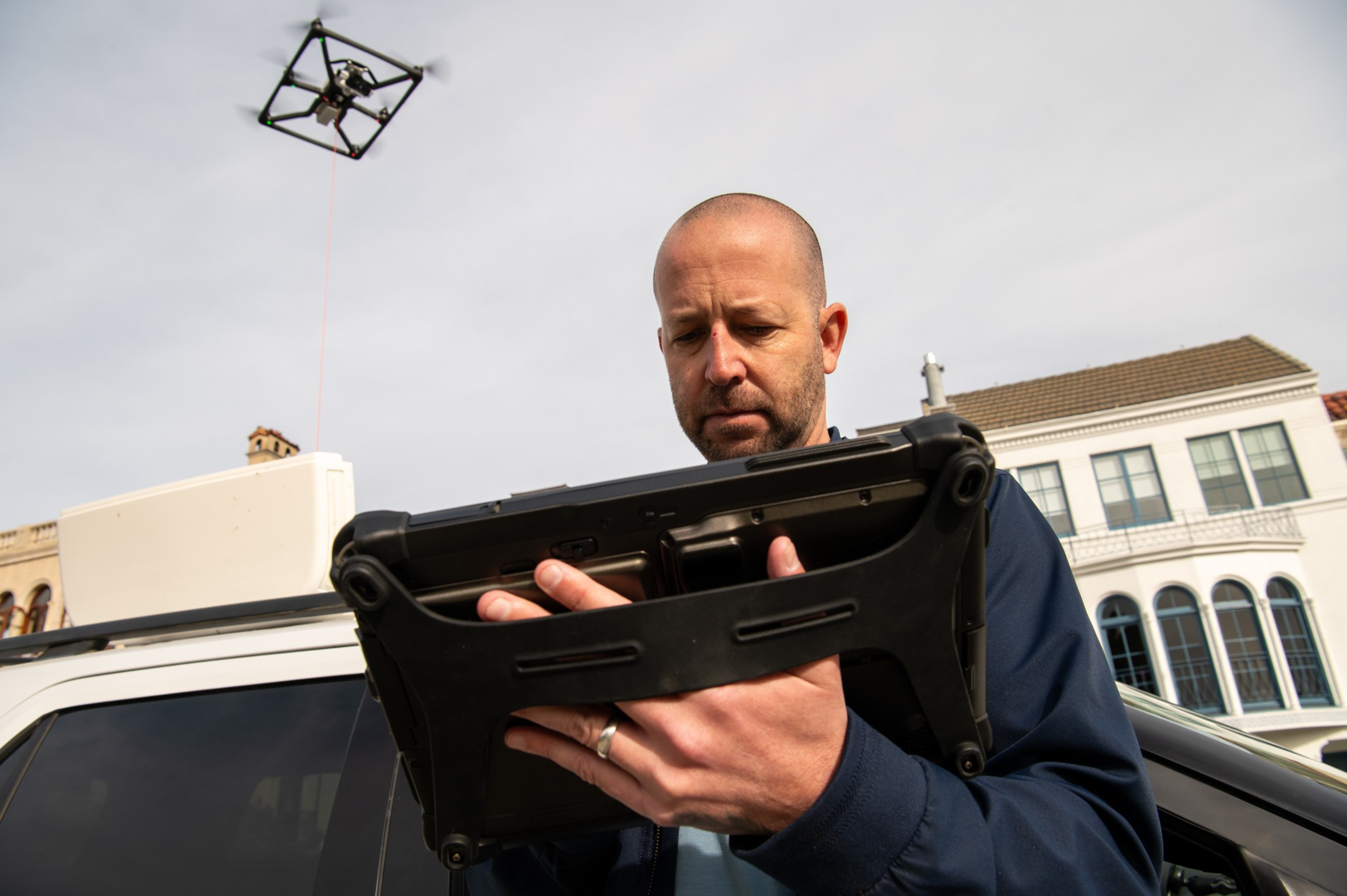 A man looks at an ipad with a drone in the background.
