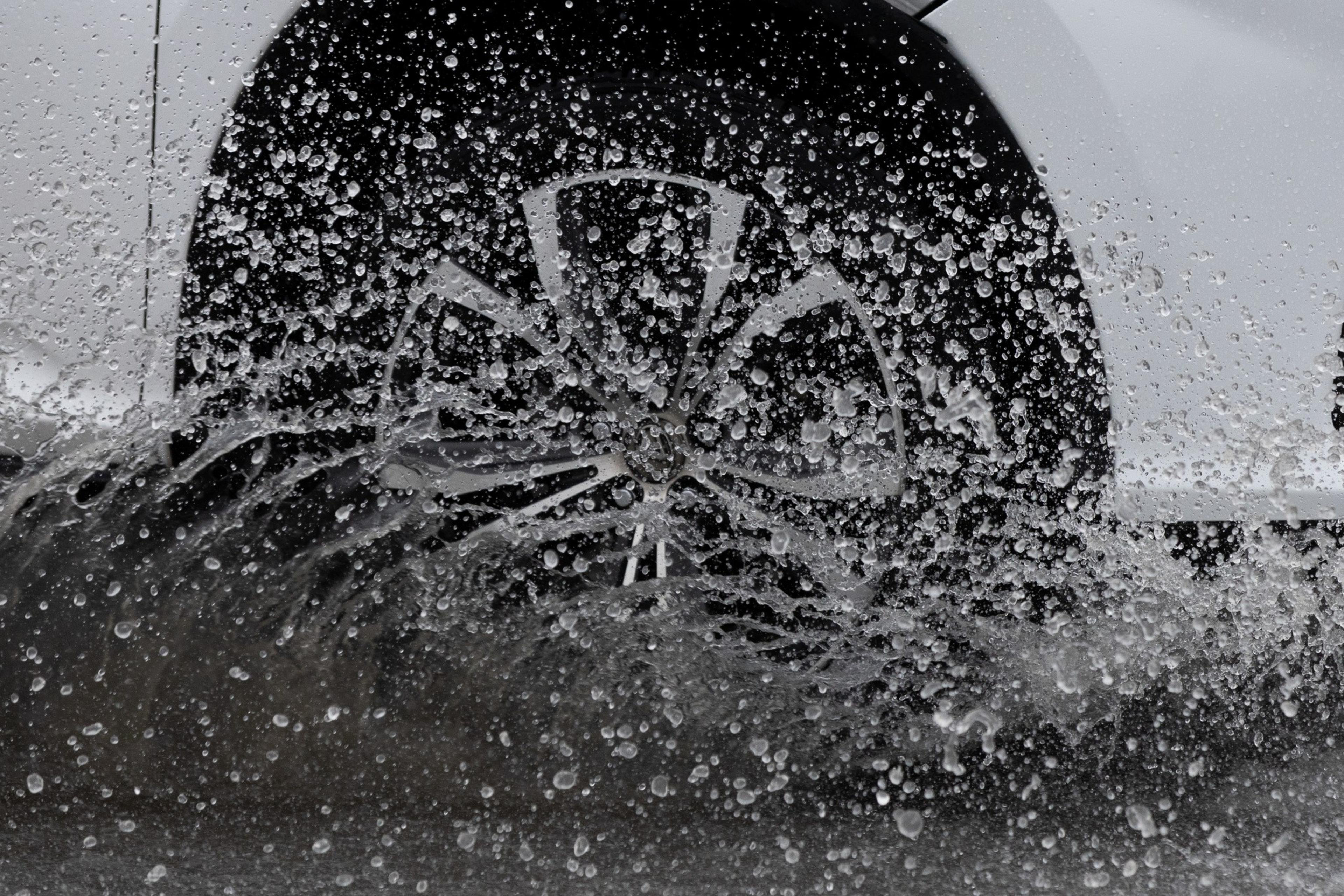 A car wheel is splashing through water, droplets frozen in motion.