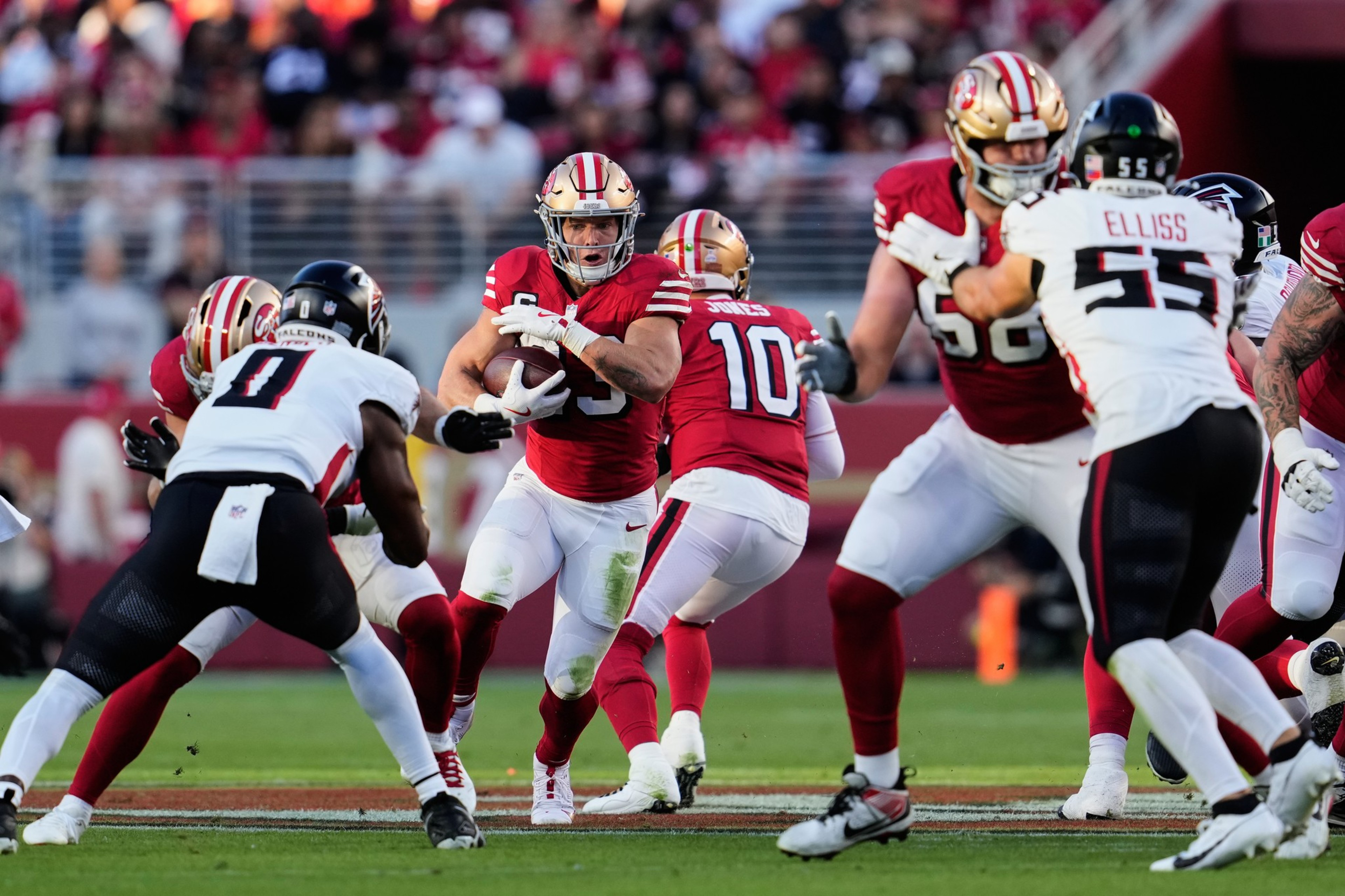 A football player in red carries the ball while teammates block players in white trying to tackle him during a game.