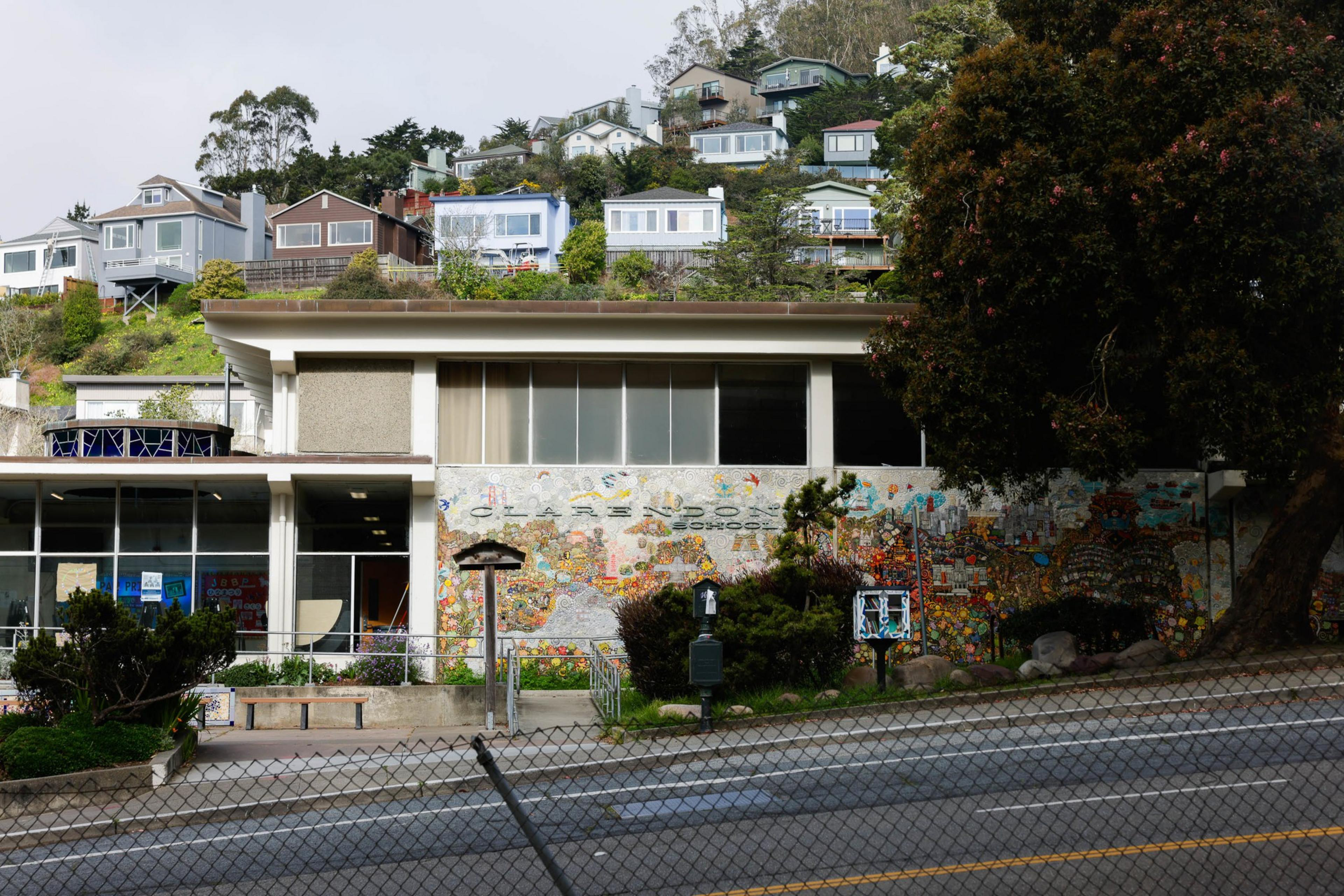 A school with a colorful mosaic façade sits below a hillside dotted with houses.