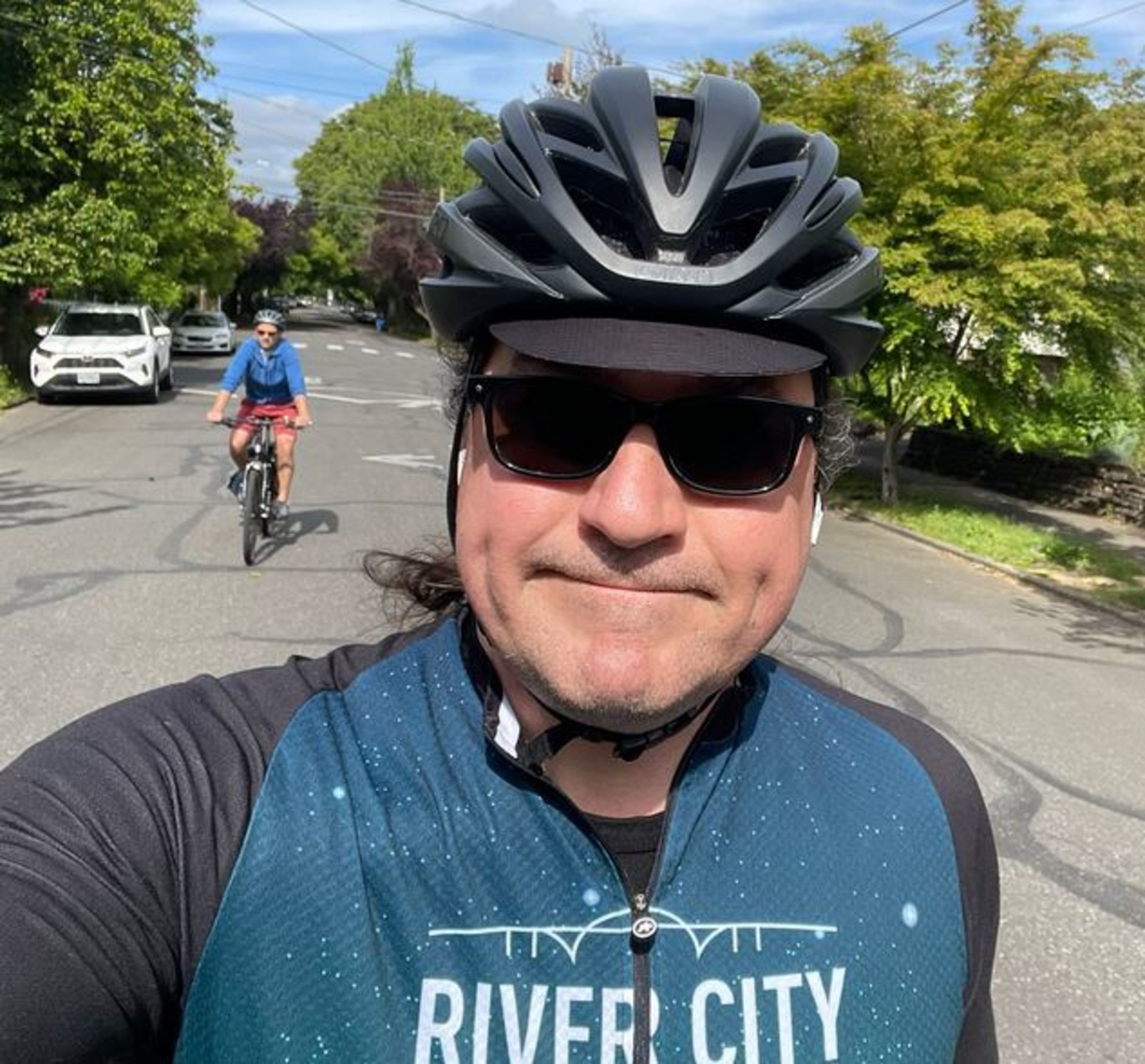 A man wearing a bike helmet and sunglasses stares into the camera.