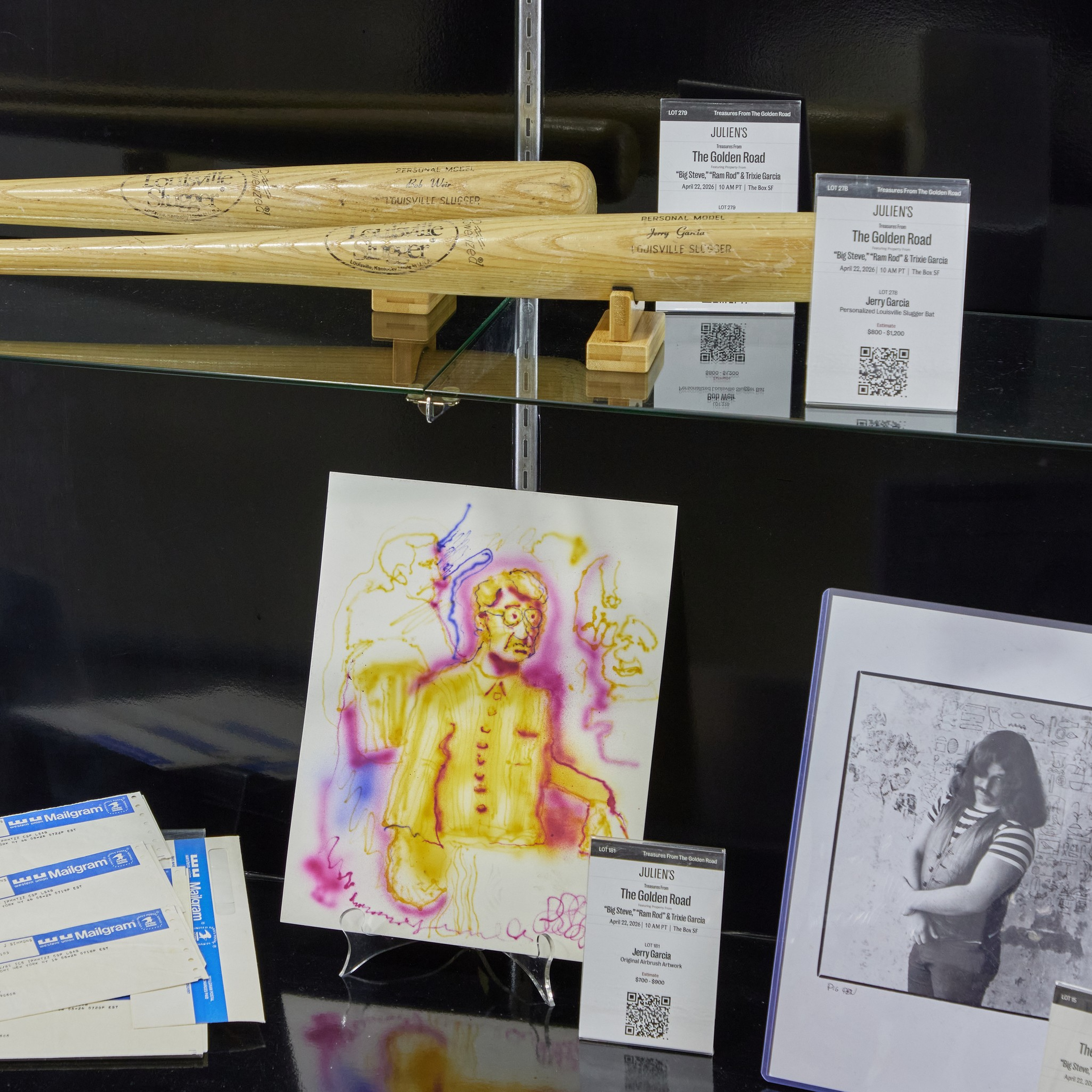 Two wooden baseball bats rest on stands with auction info cards. Below are colorful artwork of a man and a black-and-white photo of a person with long hair.