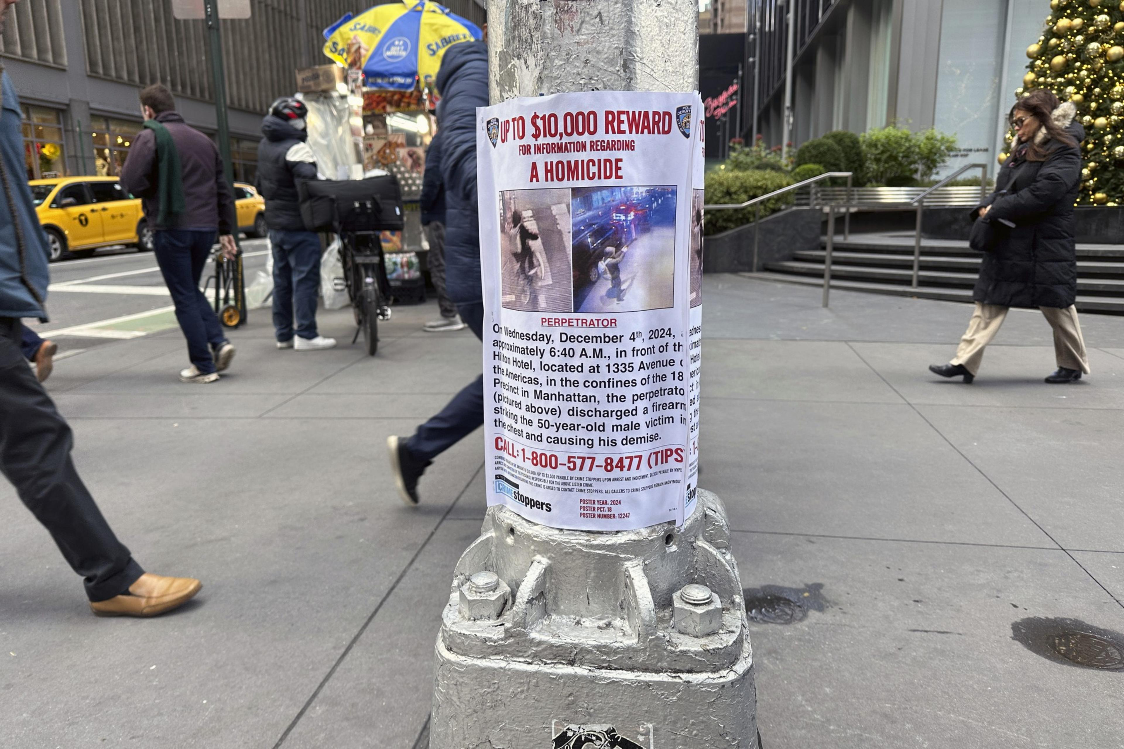 A reward poster on a pole offers up to $10,000 for information on a homicide. It includes images of the suspect and details about the incident, with a tip line number.