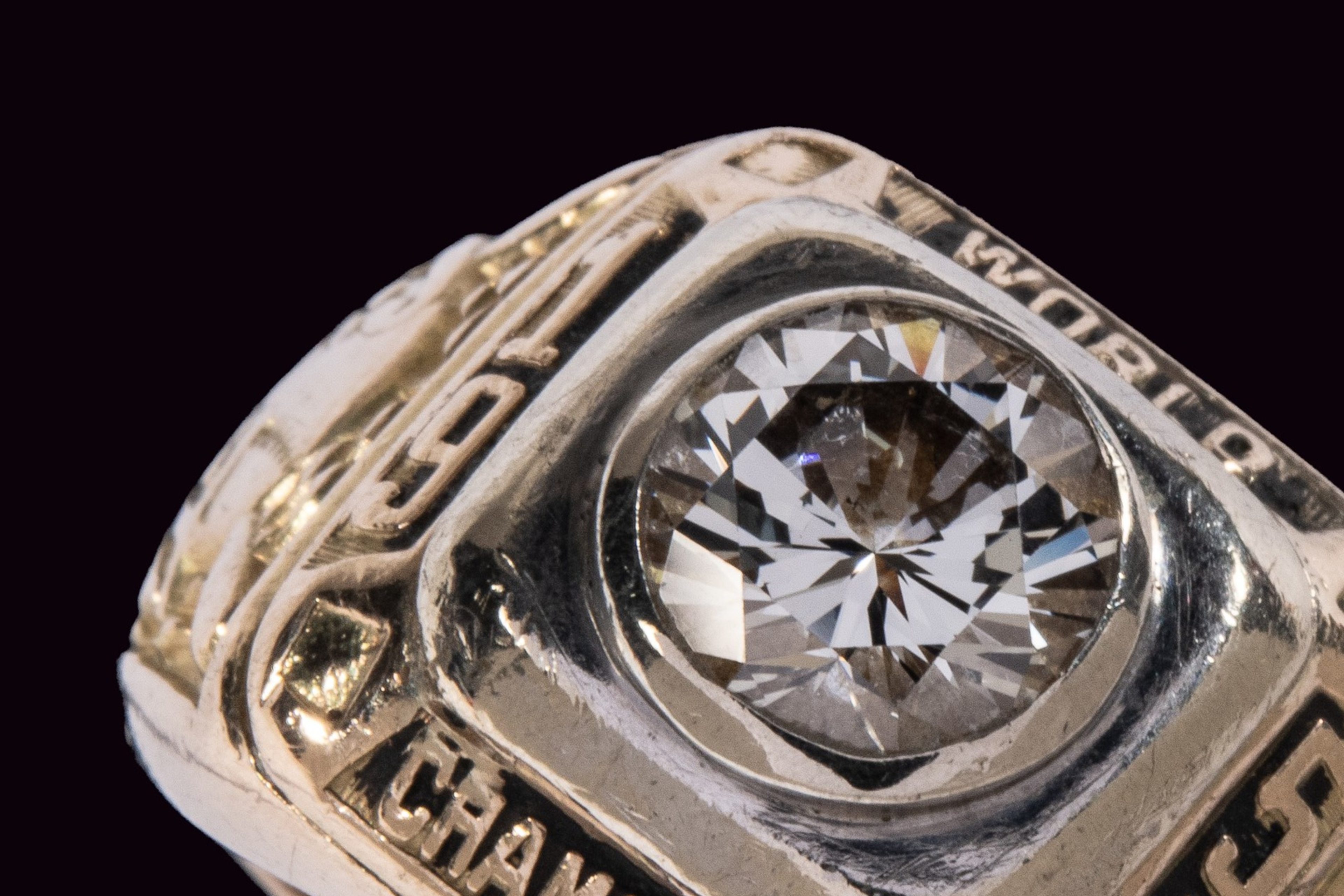 The image shows a gold championship ring with a large central diamond. It has the words "World Champions" engraved around the diamond.