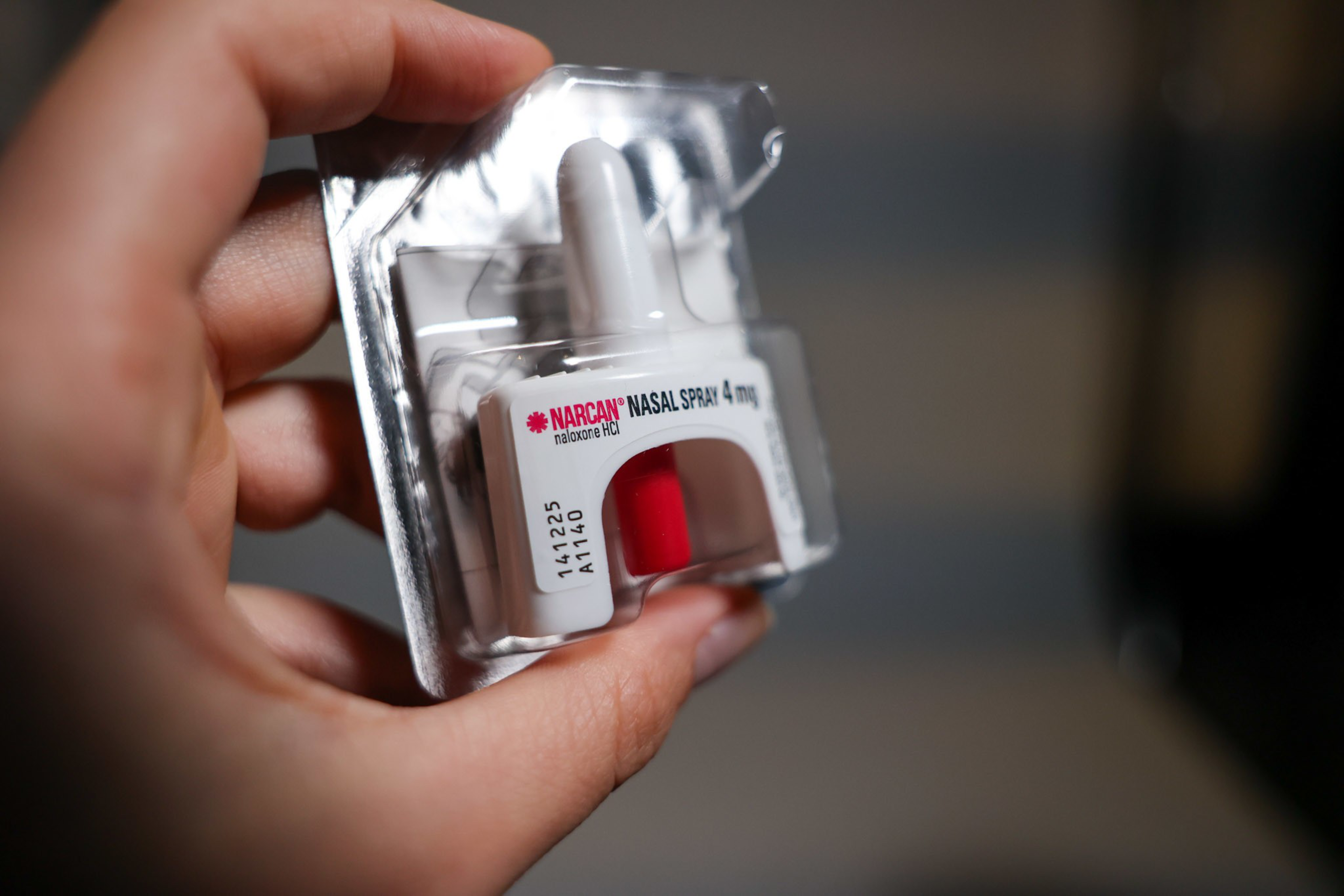 A hand holds a packaged Narcan nasal spray, a medication used to reverse opioid overdoses.