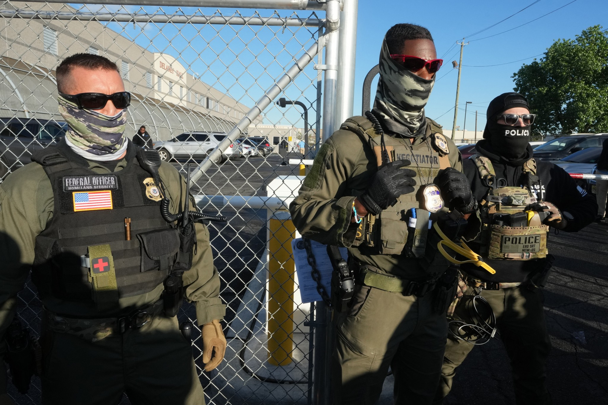 Three masked ICE agents stand in front of fence