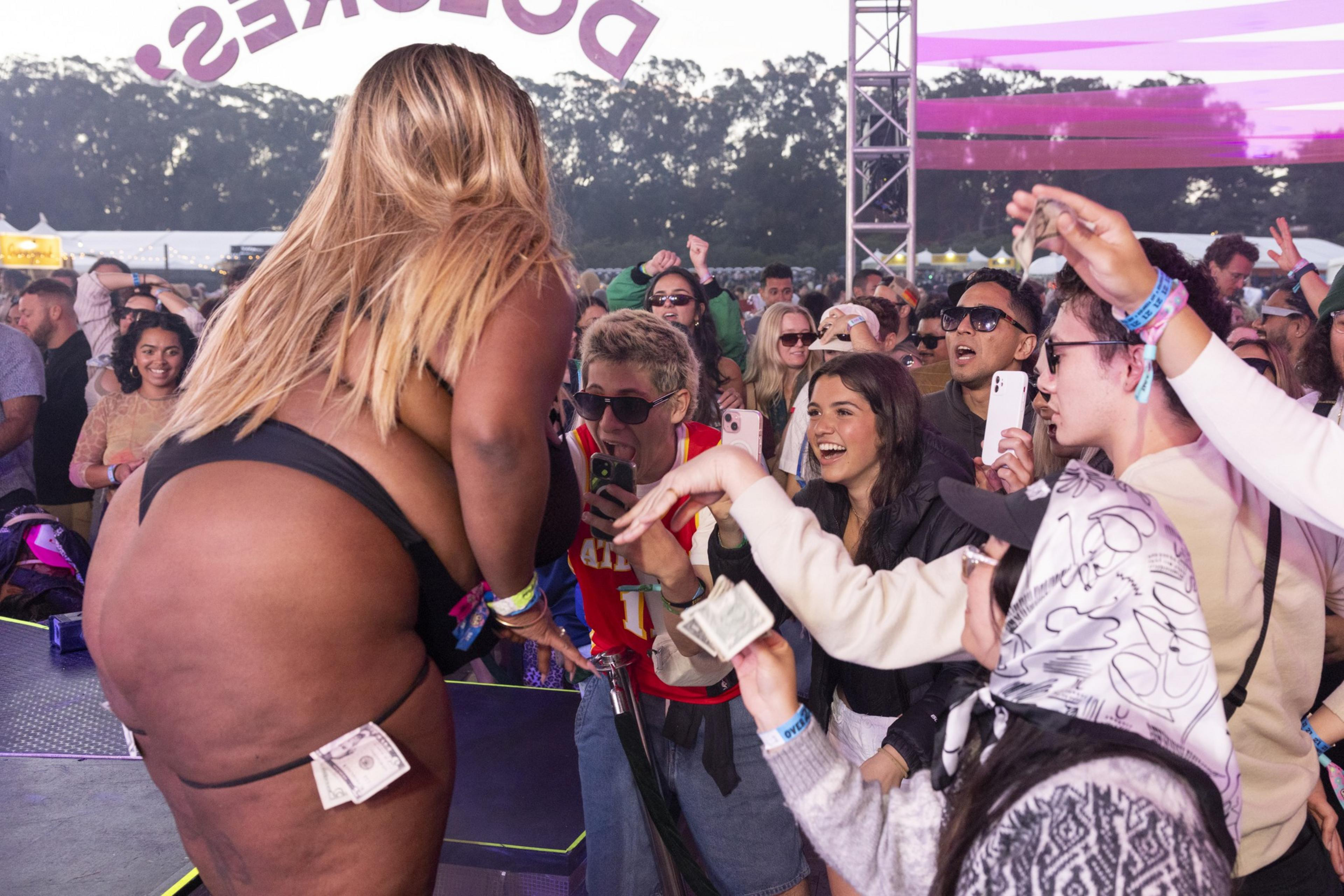 A performer in black underwear dances on stage while a cheering crowd holds up phones and money, creating a lively and excited atmosphere.
