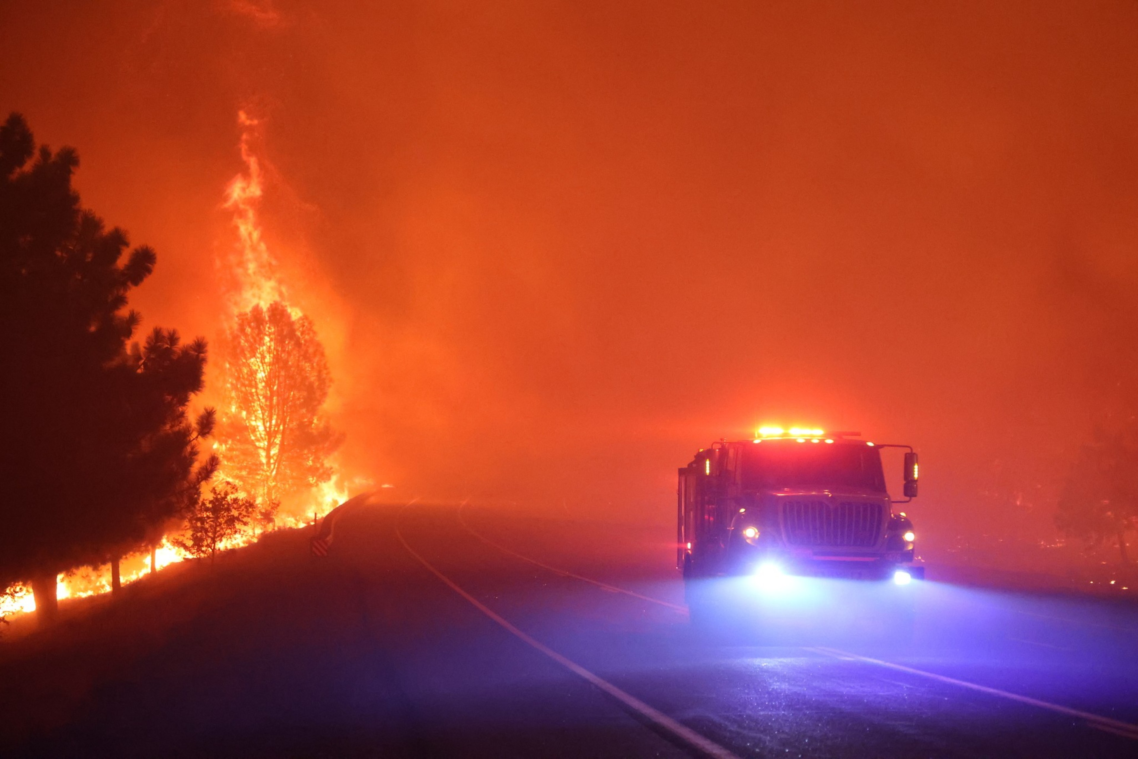 An emergency vehicle drives through a fire-lit road.