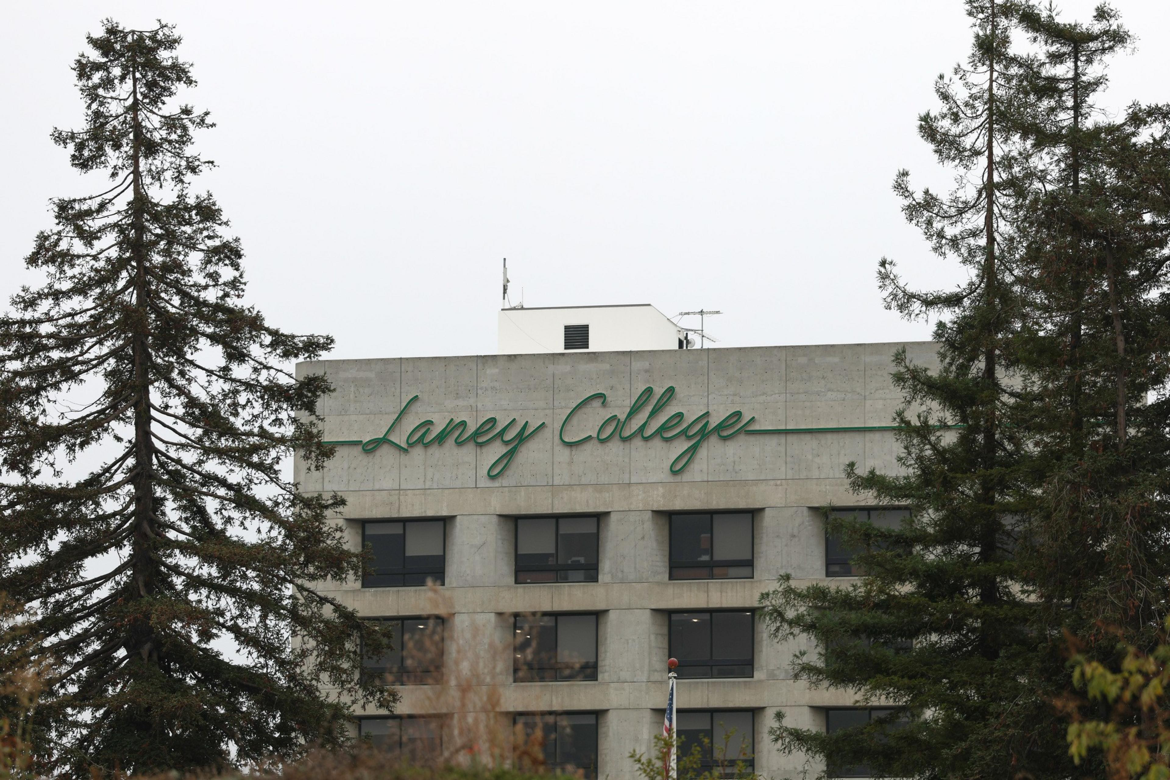 A concrete building with "Laney College" written in green cursive lettering near the top, framed by tall evergreen trees on both sides.