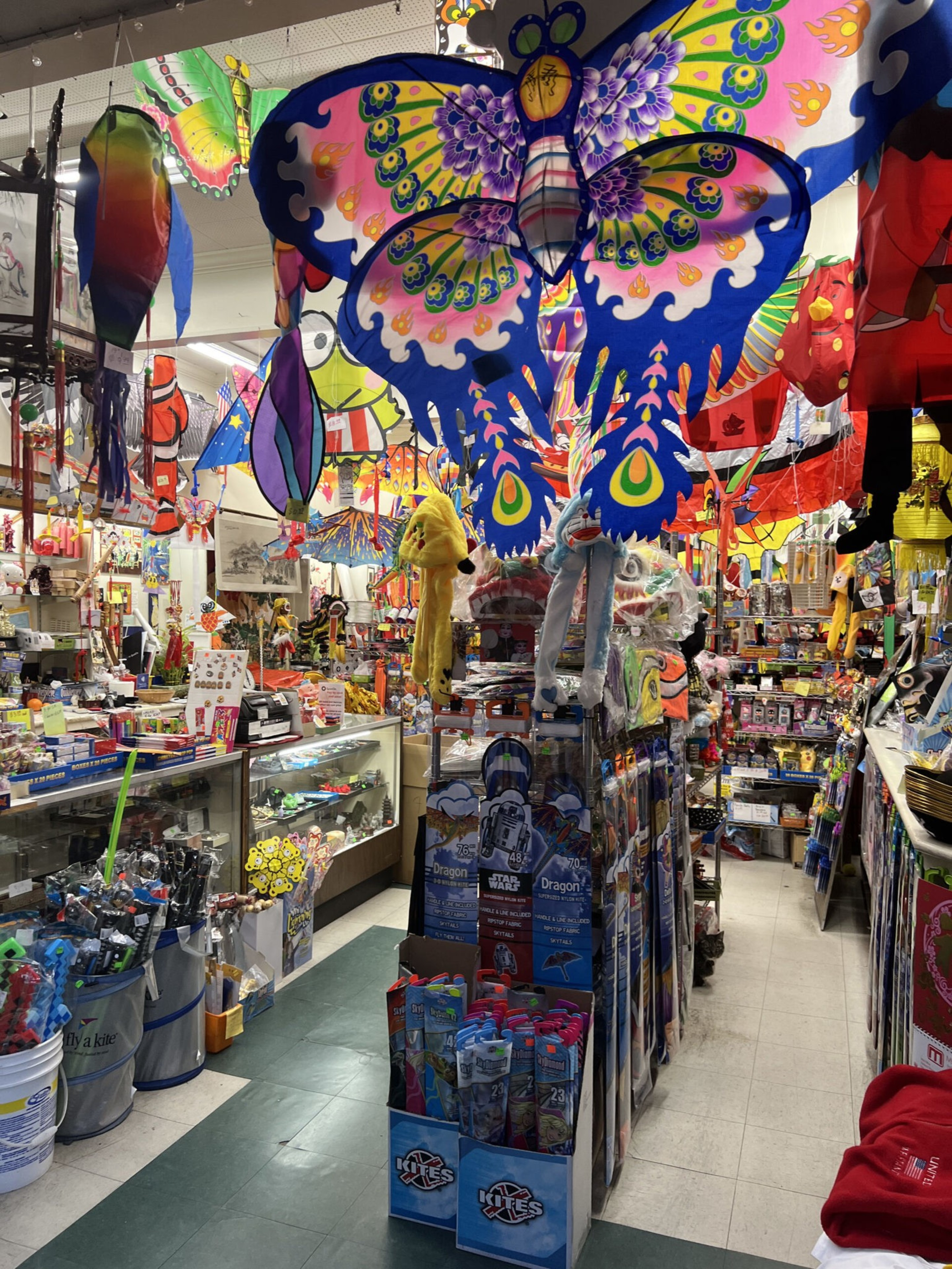 A blue and pink kite hangs in s hope crowded with kites and other merchandise.