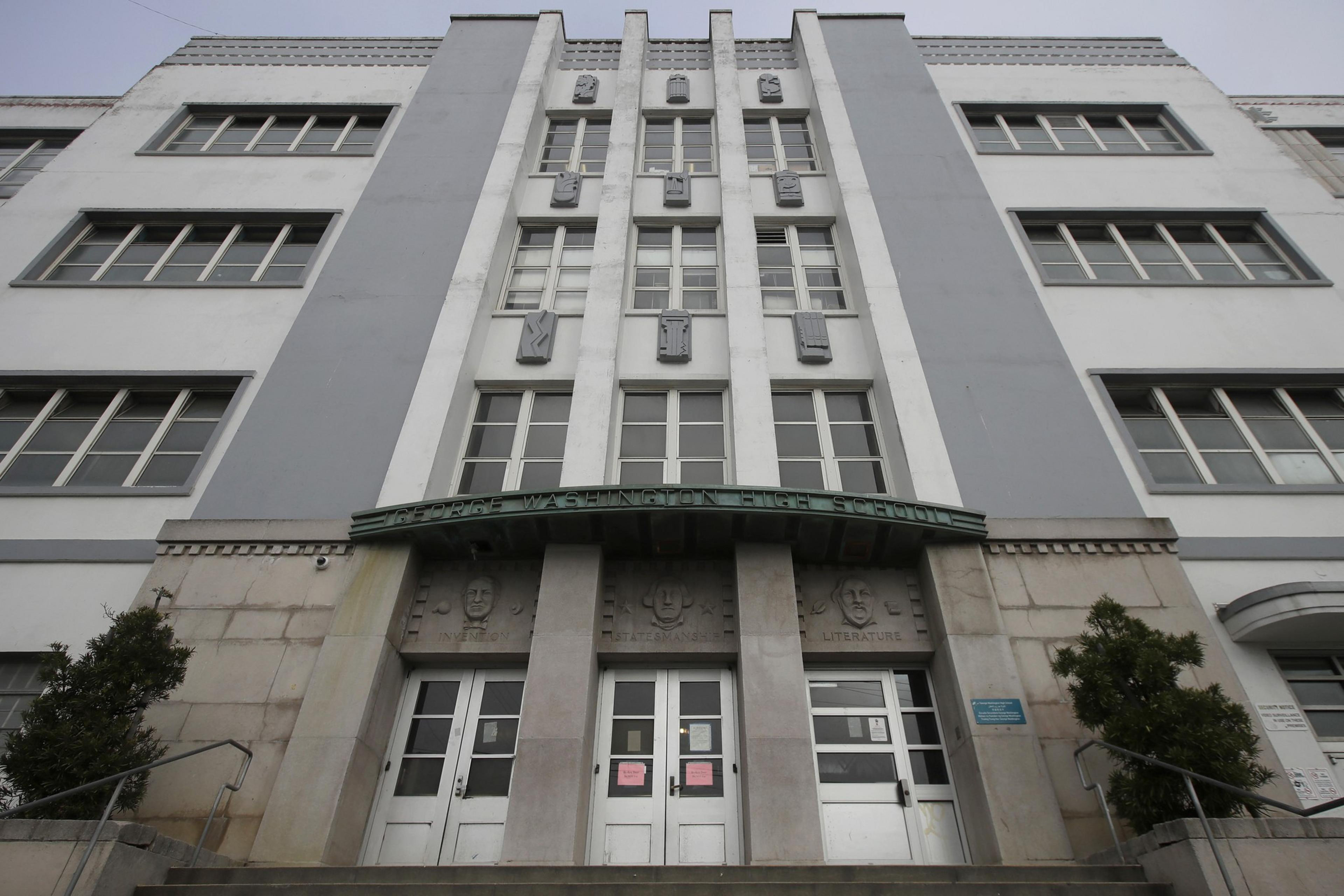 The image shows the facade of a multi-story building labeled &quot;George Washington High School.&quot; It features symmetrical windows, doors, and decorative stonework.