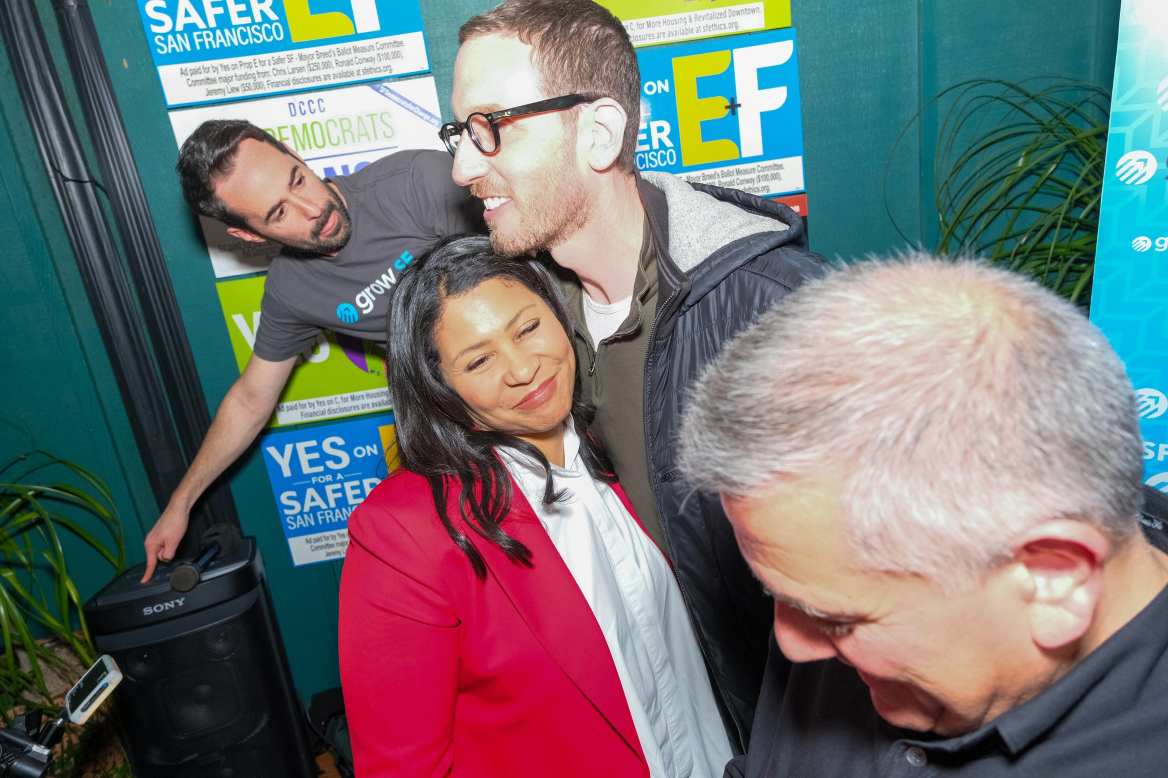Three people are huddled closely together for a selfie in front of campaign posters.