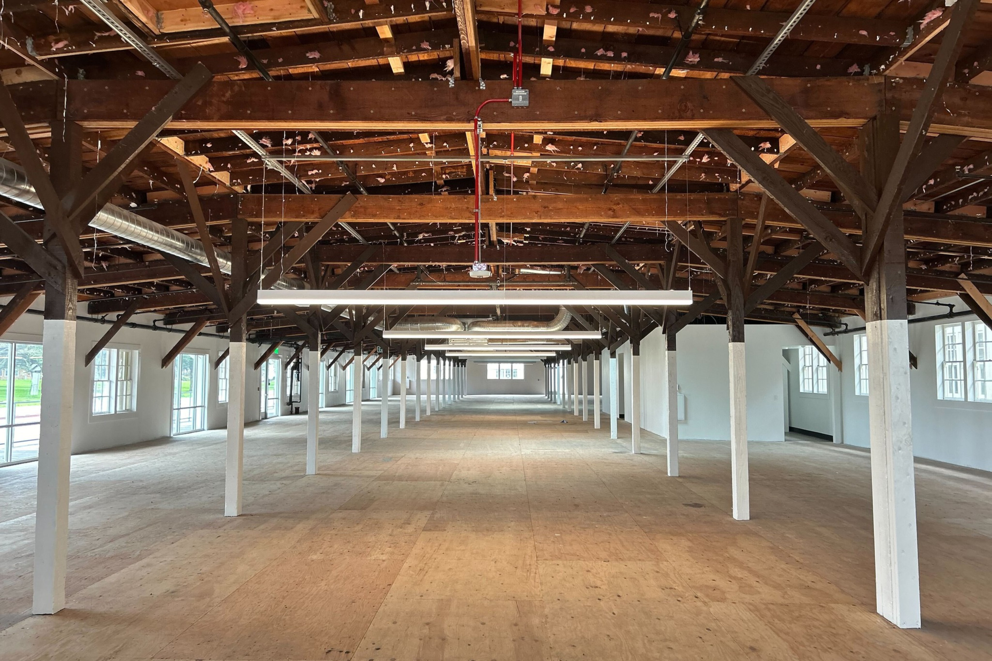 A spacious room with wooden beams on the ceiling, white columns, and large windows.