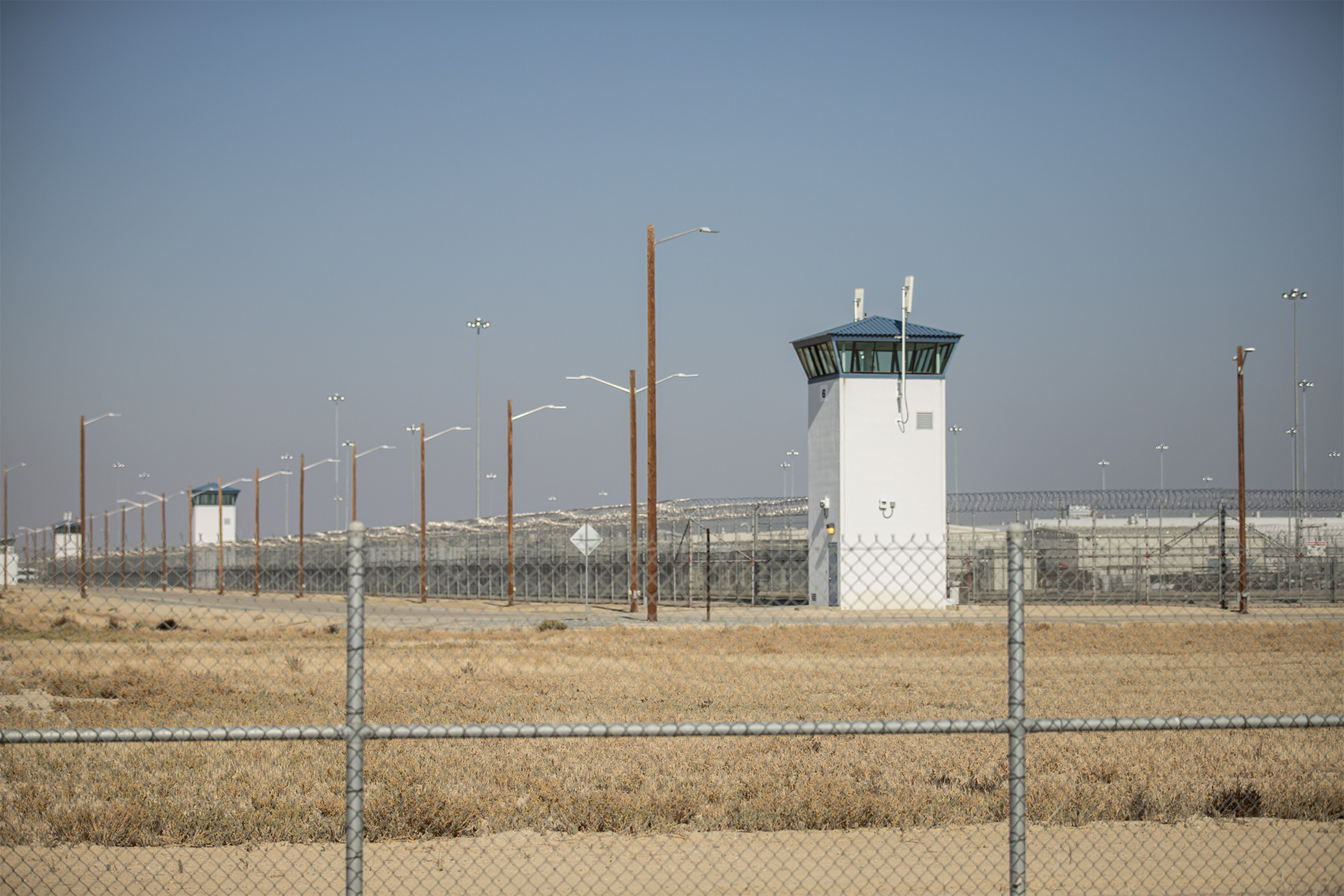 A white guard dower with a blue roof seen behind a chain link fence next in front of another fence with barbed wire