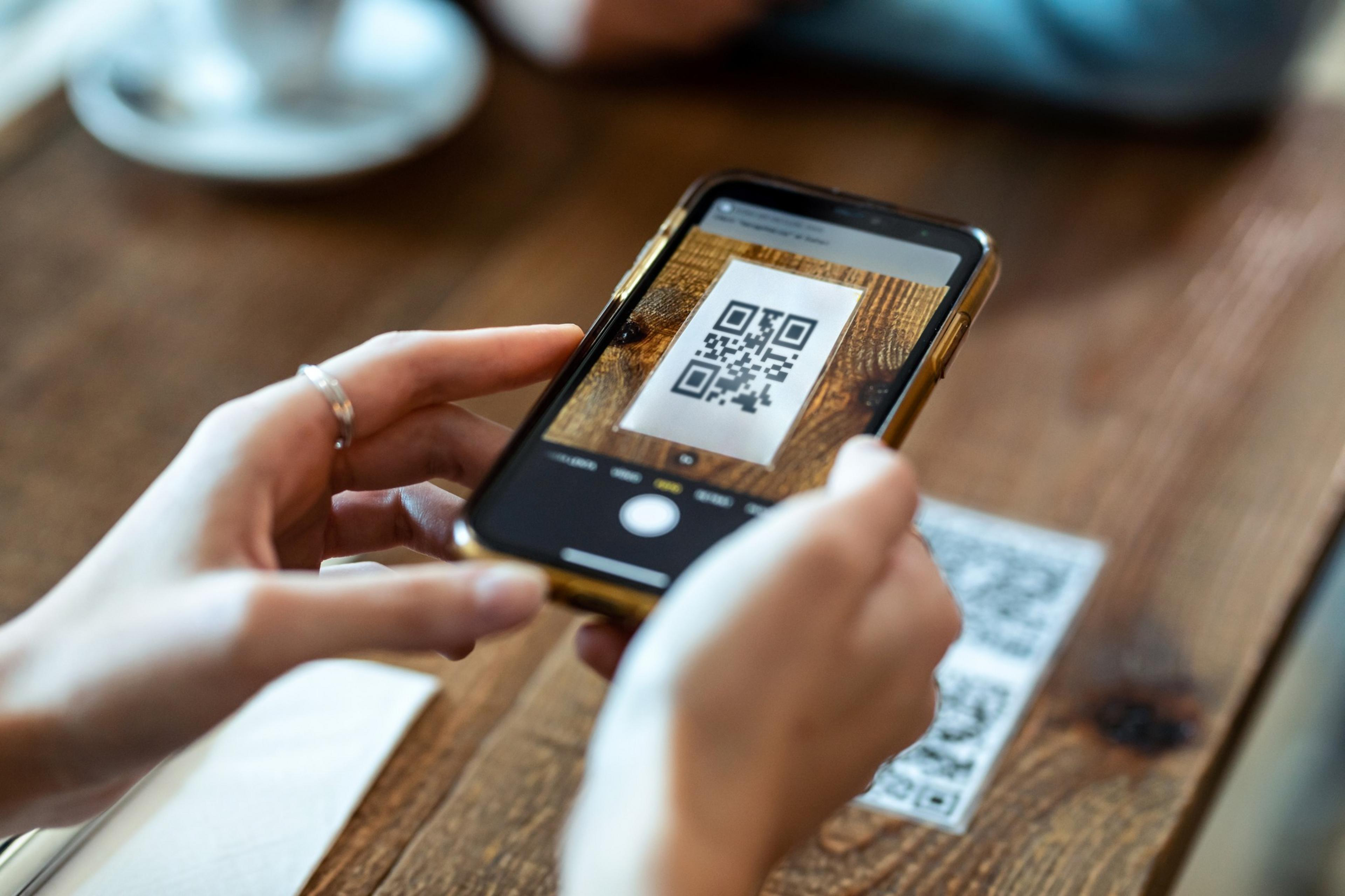 A person holding up a phone to a QR Code on a table to access the menu.