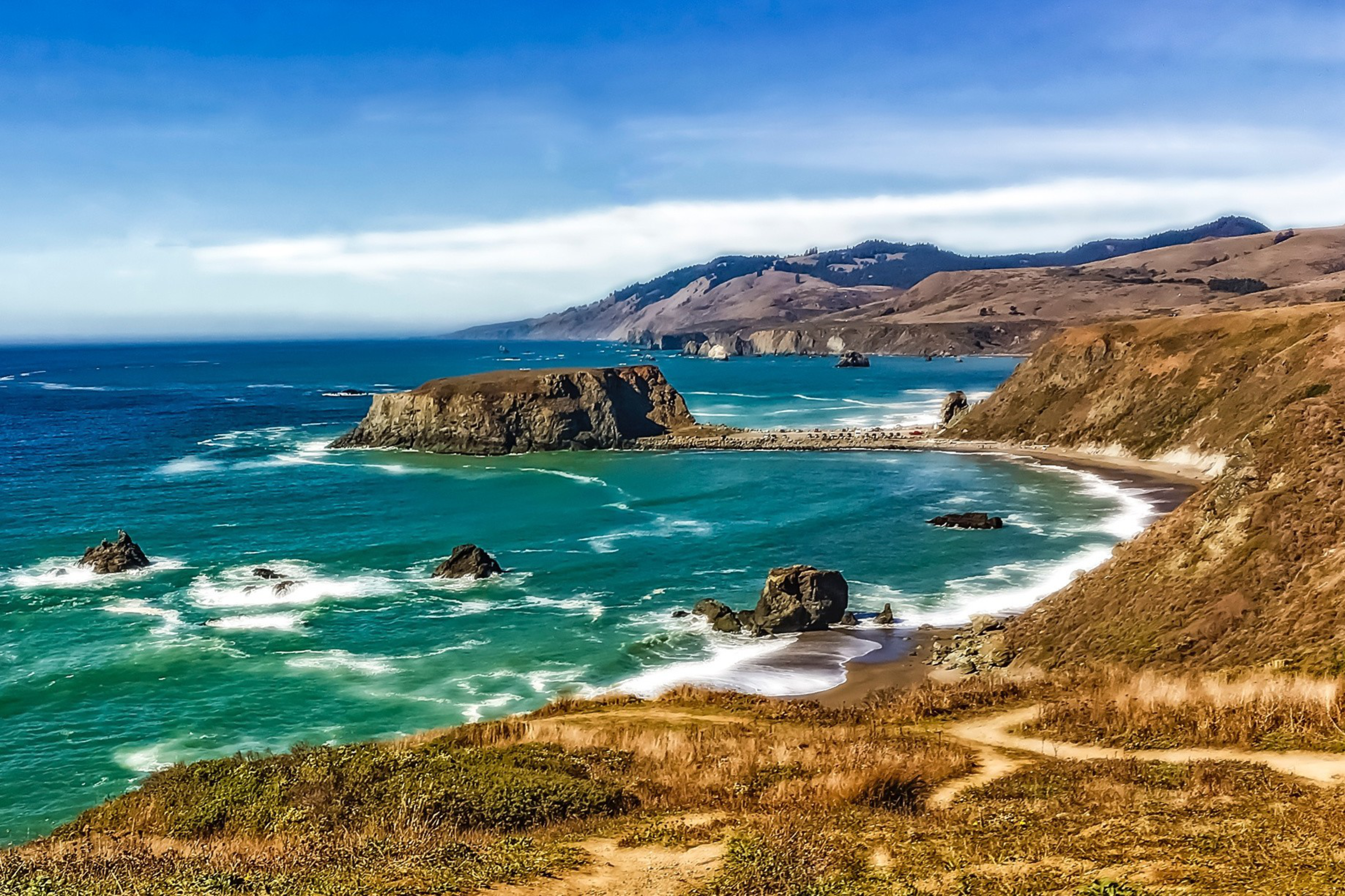 Vibrant blue waters meet a rugged ocean beach.