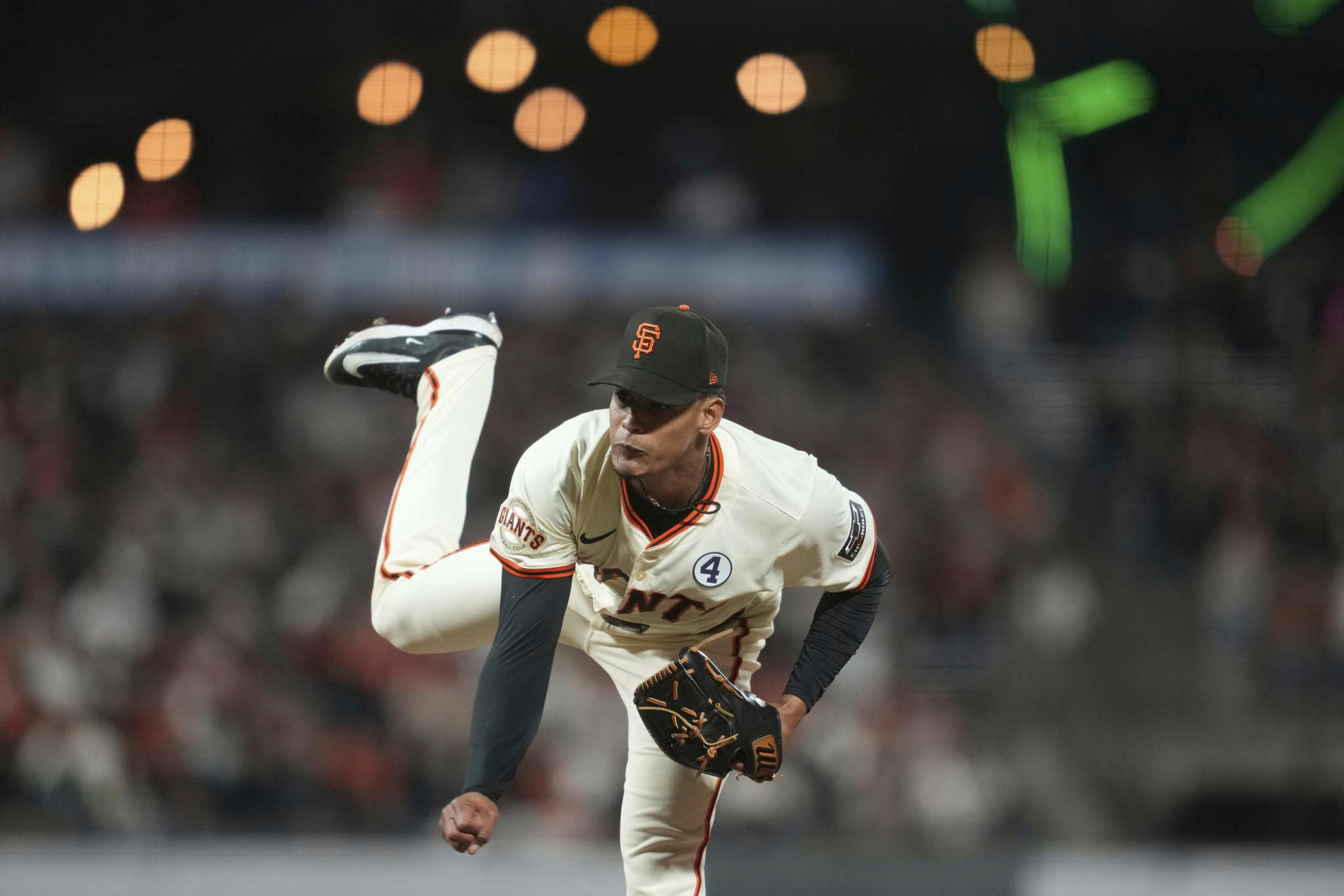 A baseball player in a white uniform with &quot;Giants&quot; lettering pitches energetically. His face is focused, cap on, as he completes a follow-through motion.