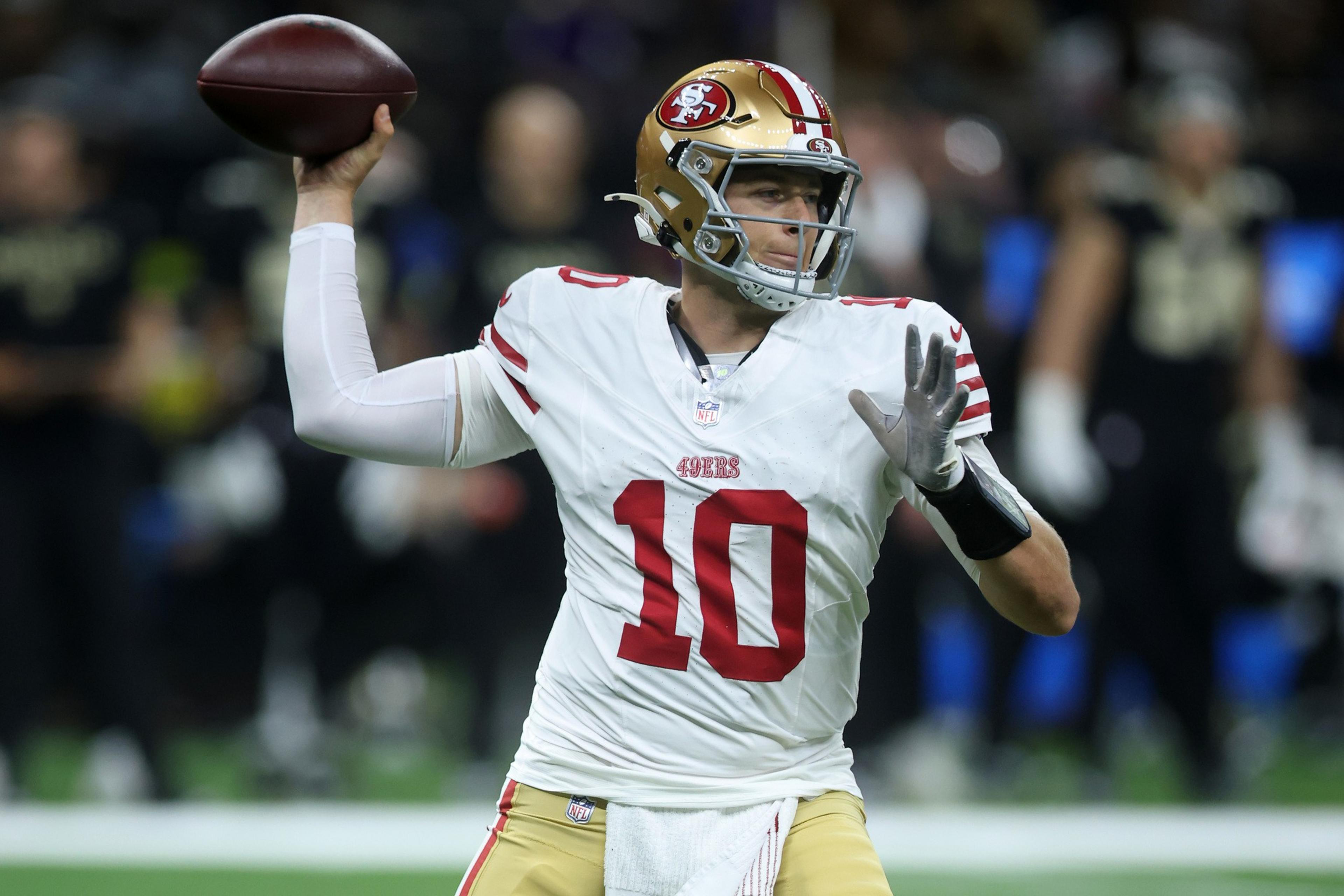 A football player wearing a white San Francisco 49ers jersey with number 10 is preparing to throw a pass during a game.
