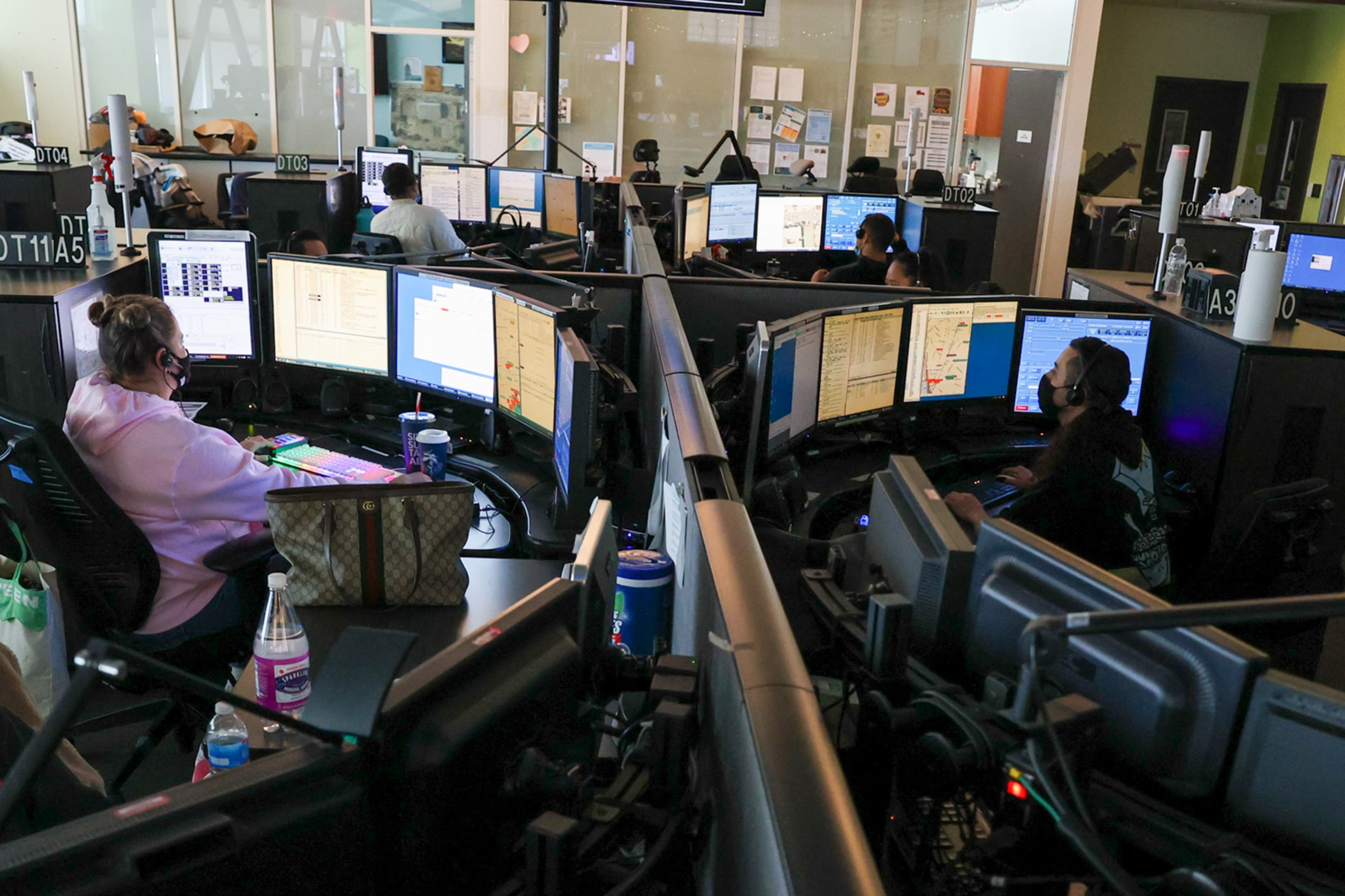 Multiple people wearing headsets work at computer stations with multiple monitors in a dimly lit, partitioned office space.