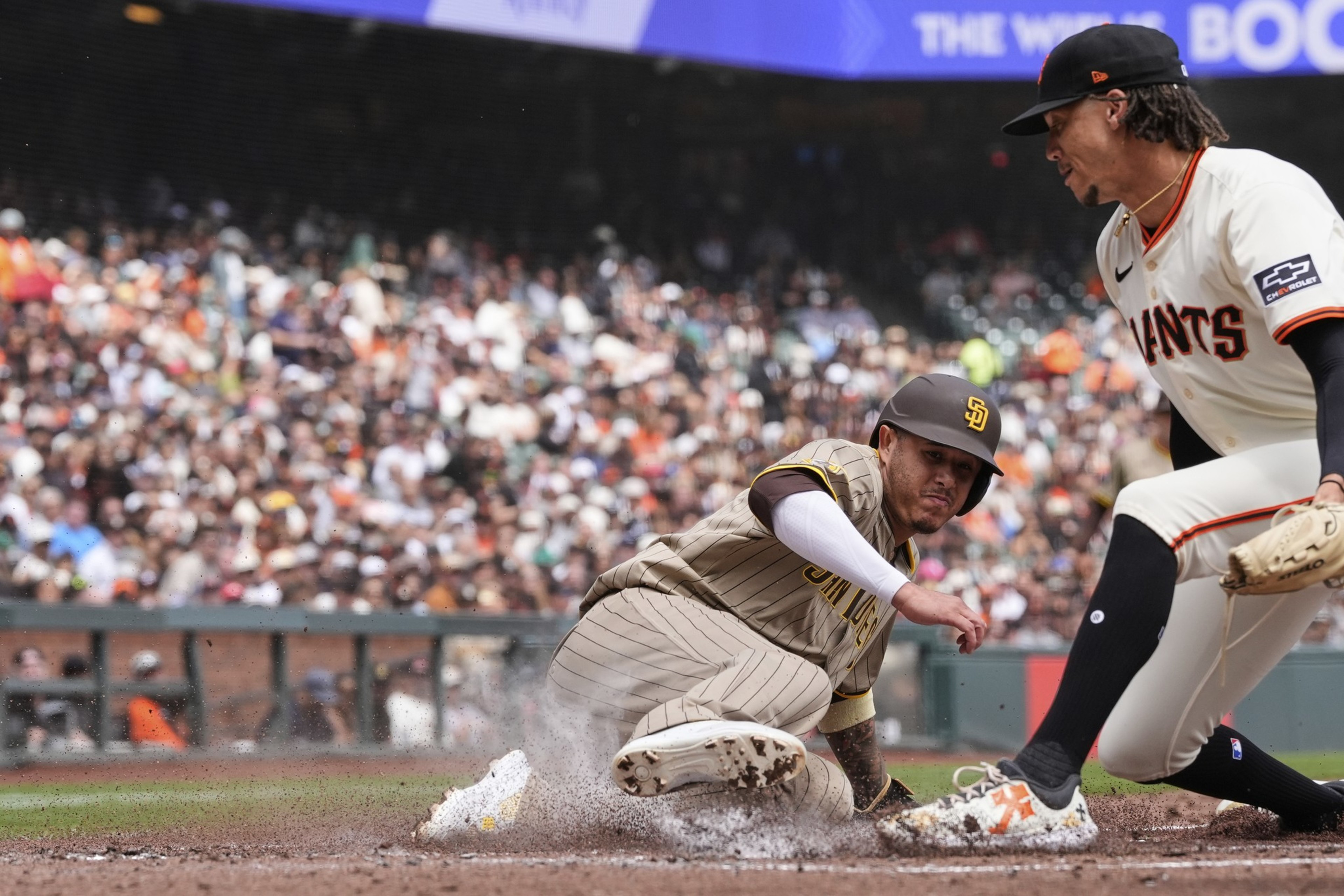 A San Diego Padres player slides into home plate while a San Francisco Giants player attempts to tag him out during a baseball game.