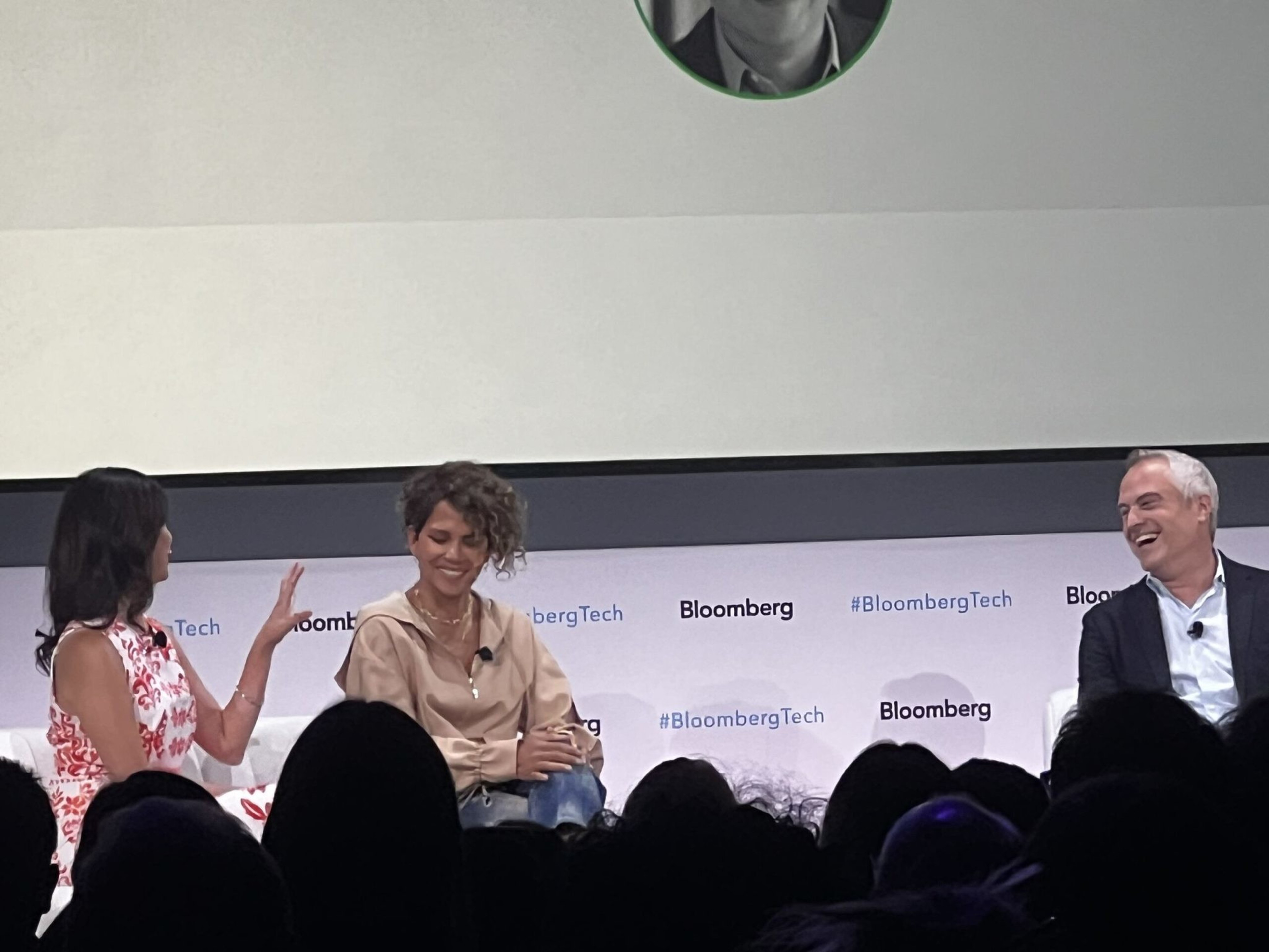 Three people sit on stage at a Bloomberg Tech event, engaged in a lively discussion, with two women and one man smiling and talking.
