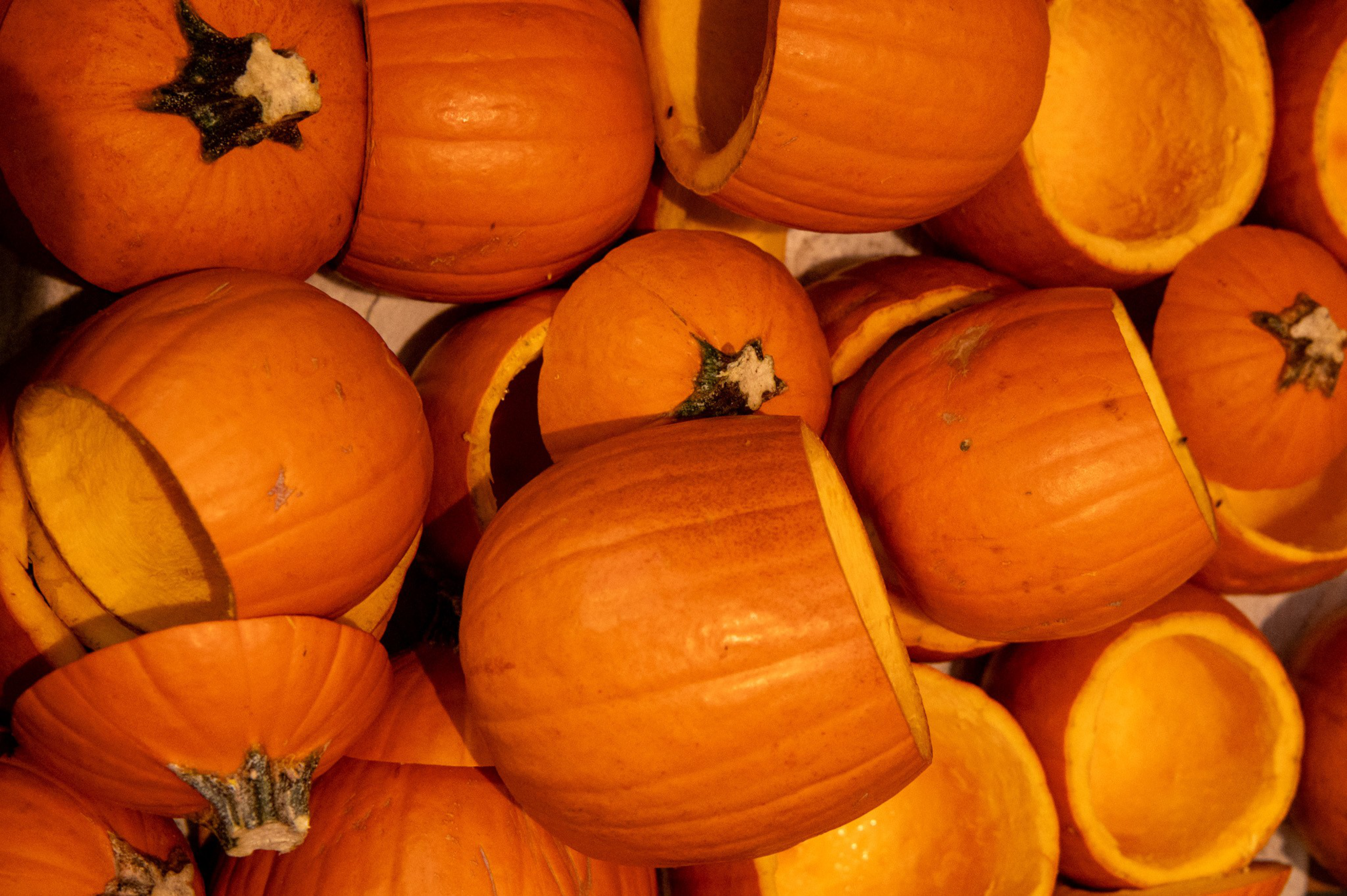 Several small to medium-sized hollowed-out orange pumpkins with their tops removed are piled together.