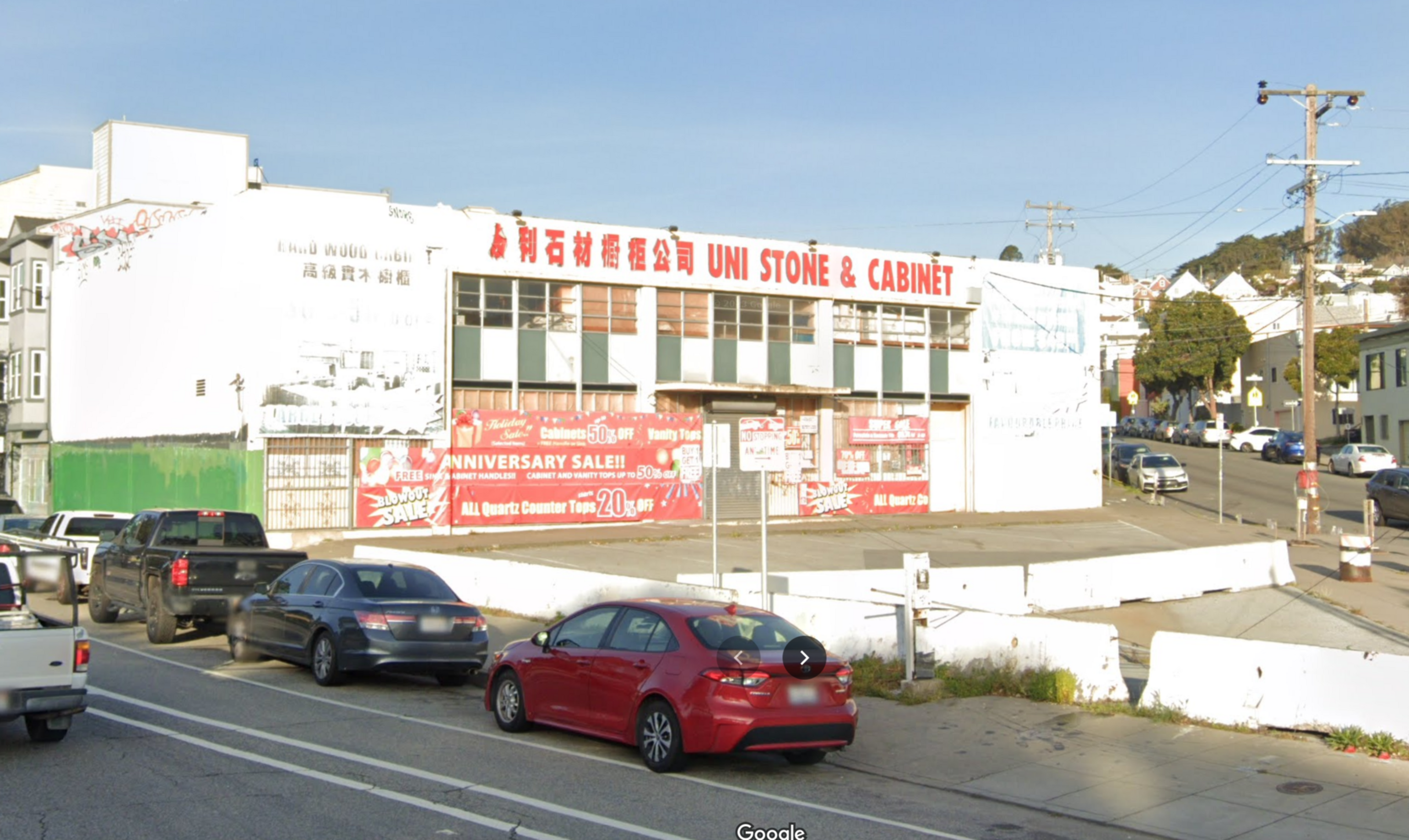 UNI Stone & Cabinet store with large red sale banners on the building, parked cars along the street, and a sunny sky above.