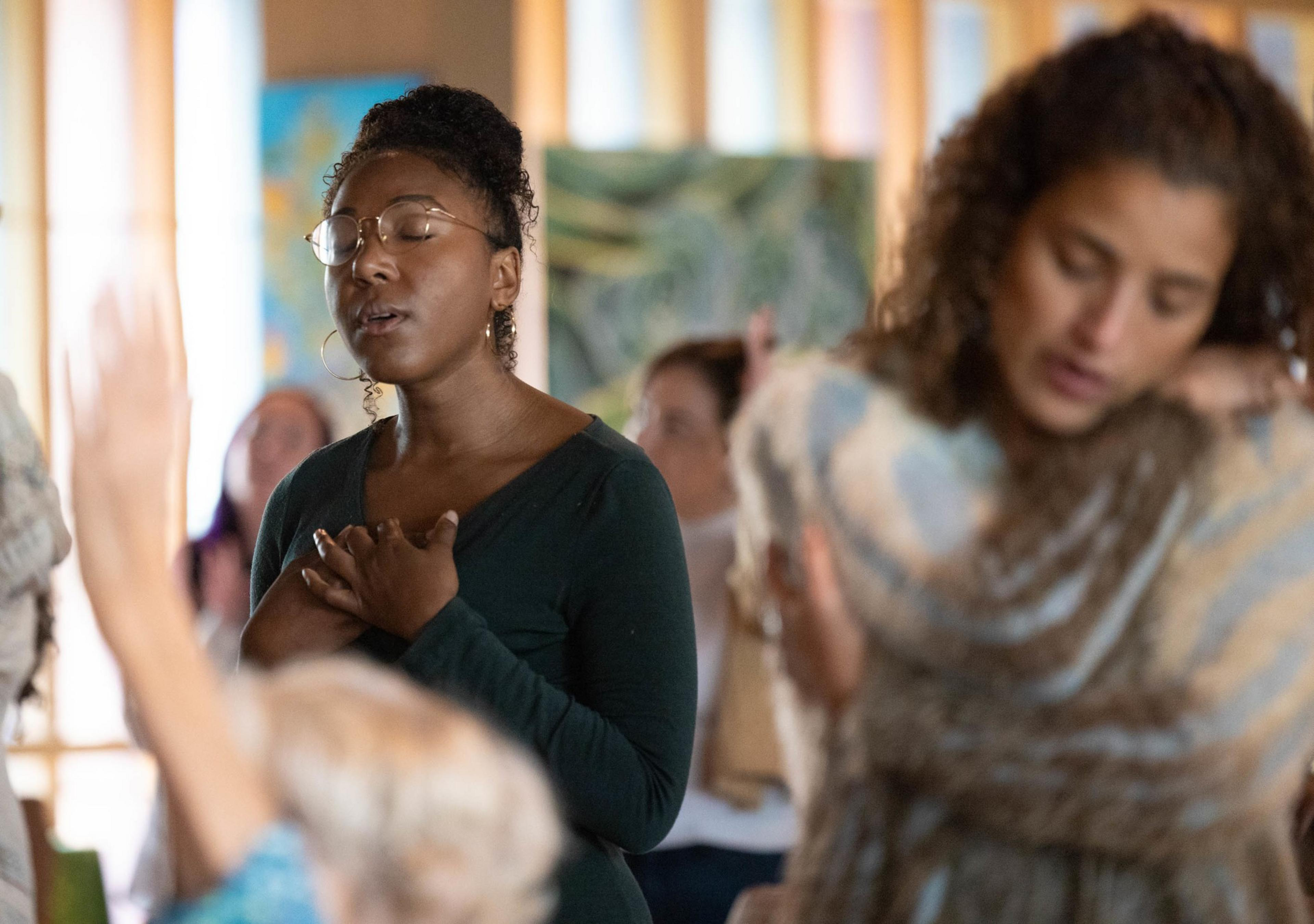 2 woman sing while hugging themselves during a church service