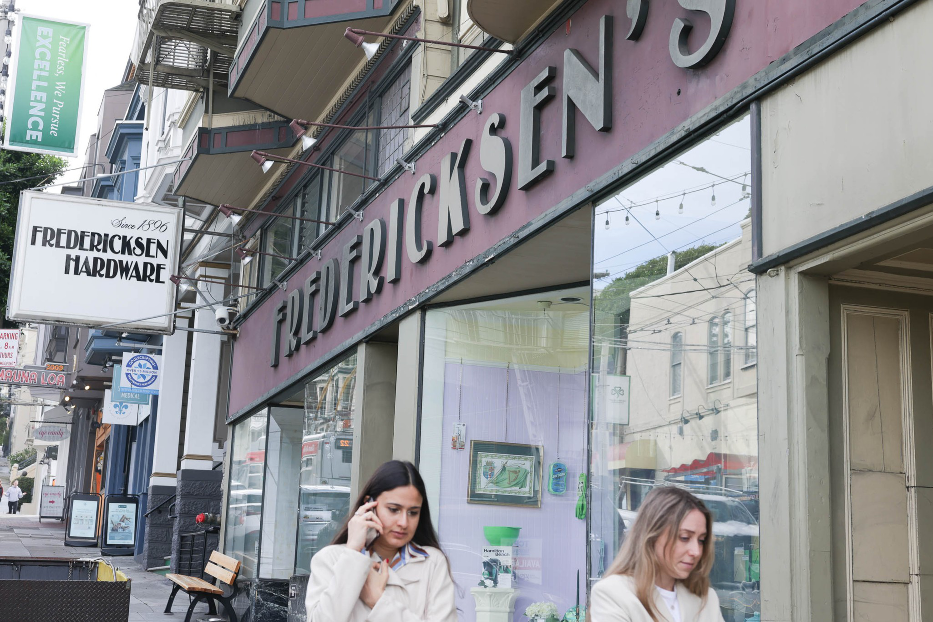 People walk by the storefront of a hardware store