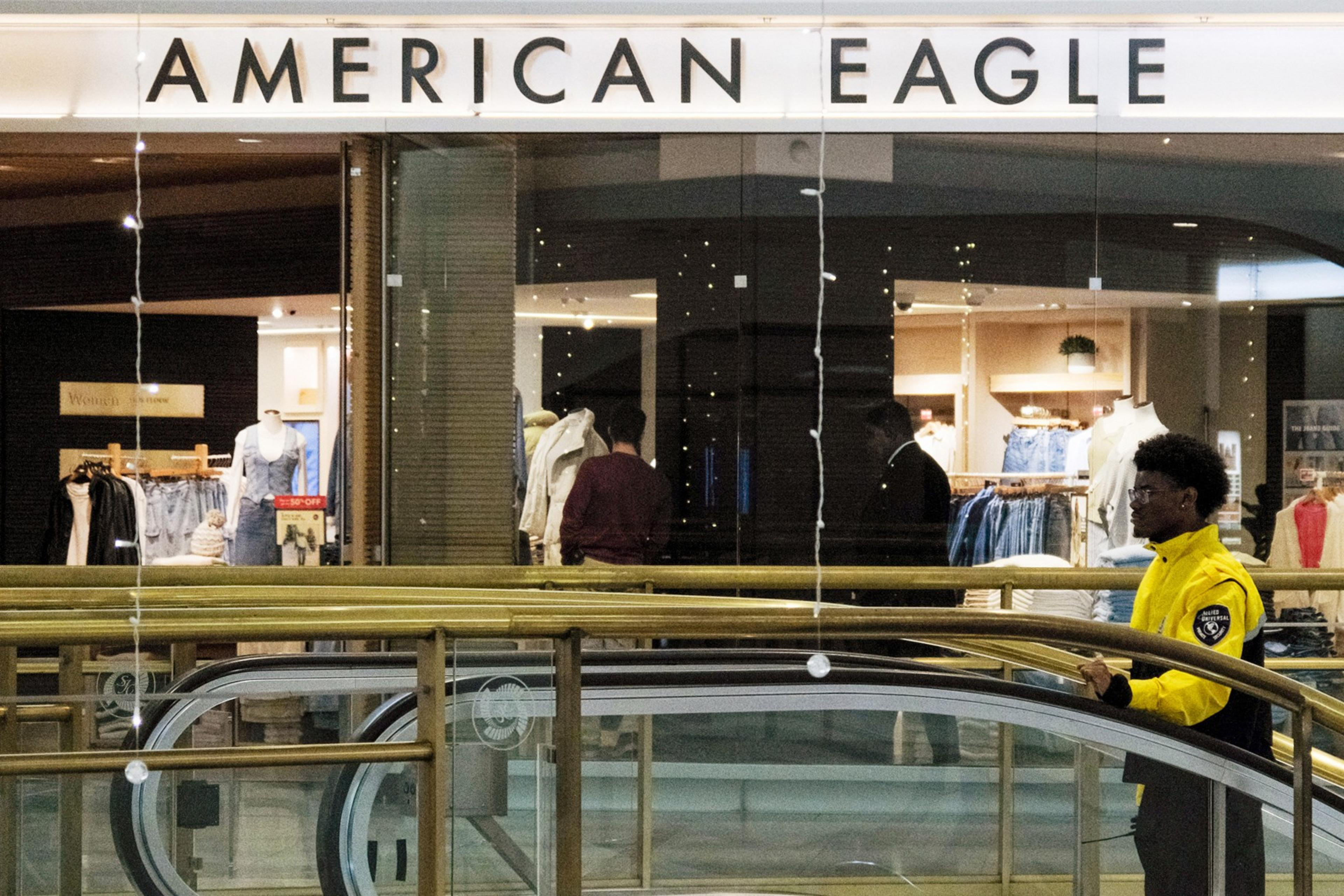 A security guard in a yellow jacket patrols near an American Eagle store in a shopping mall.