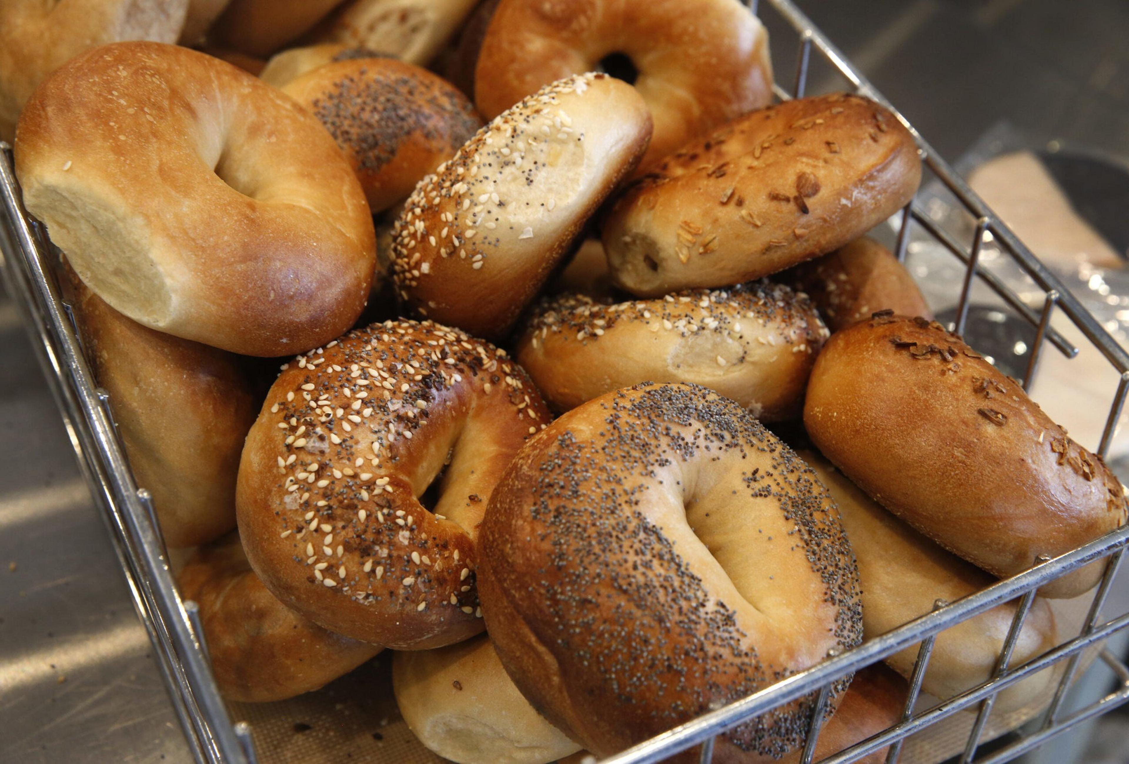 A basket filled with a variety of bagels, some topped with sesame seeds, poppy seeds, and onion flakes.