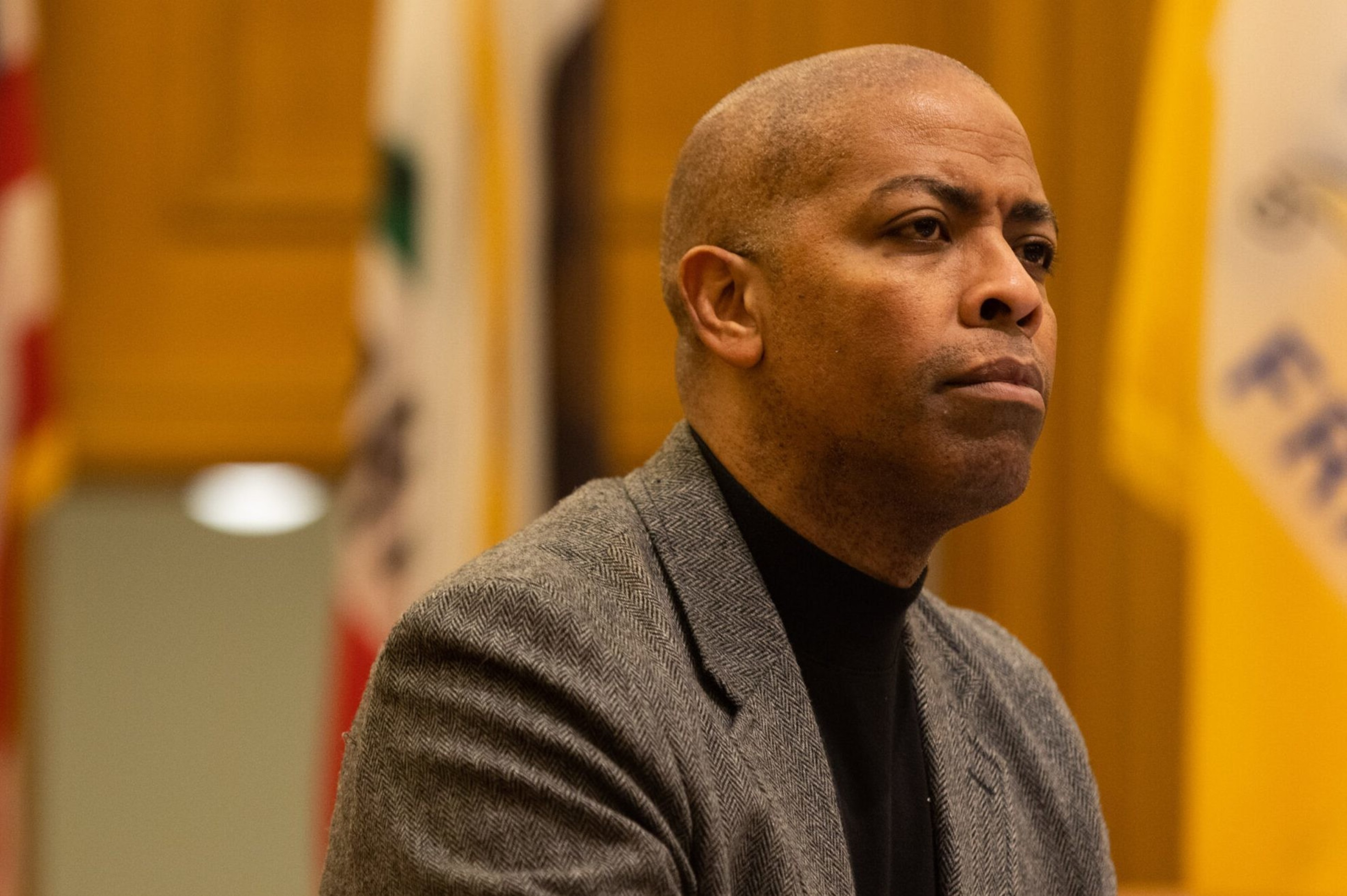 A man in a coat sits at a commission hearing.