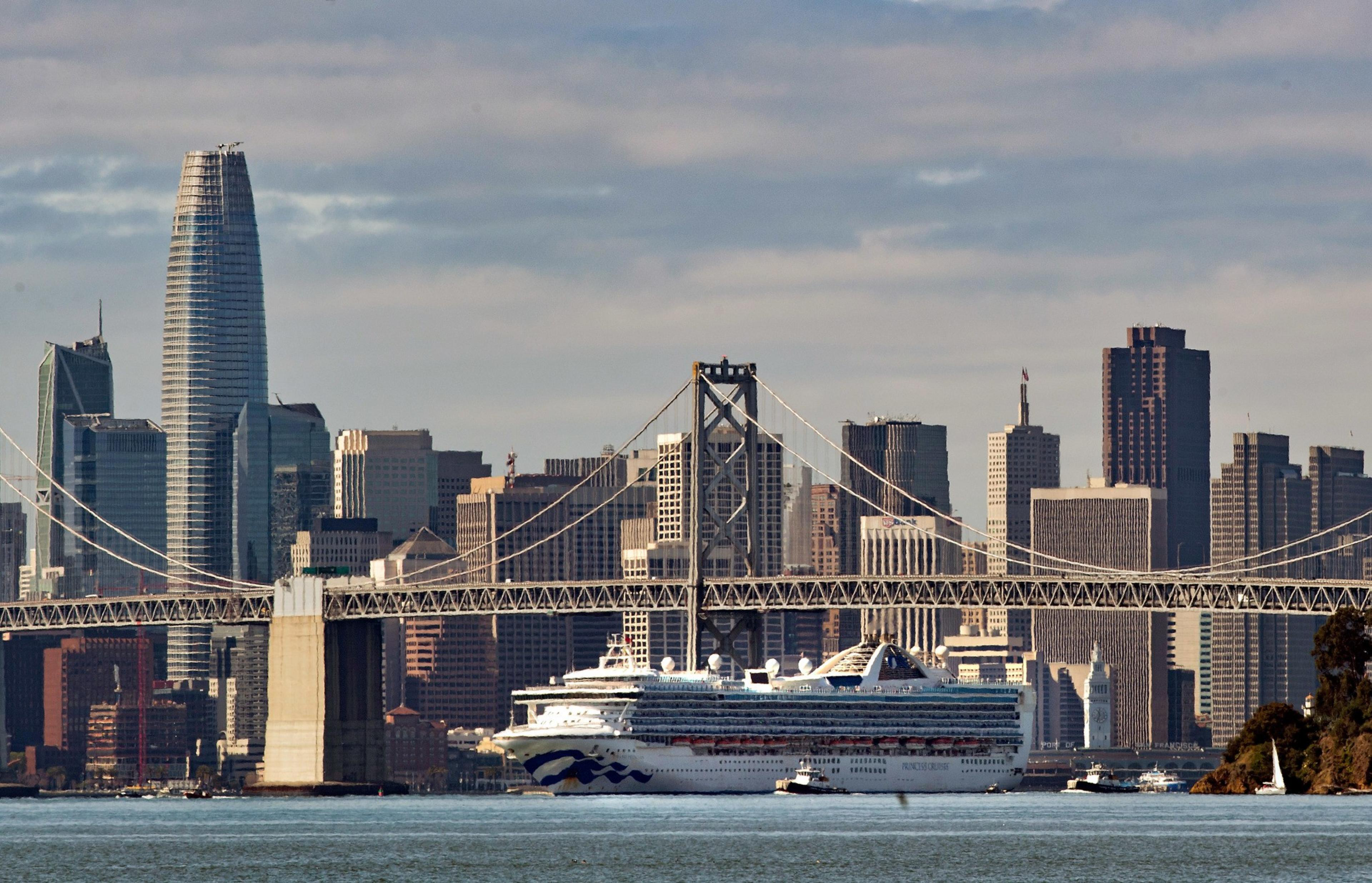 Skyscrapers with a bridge and a ferry boat on a river in the foreground. 