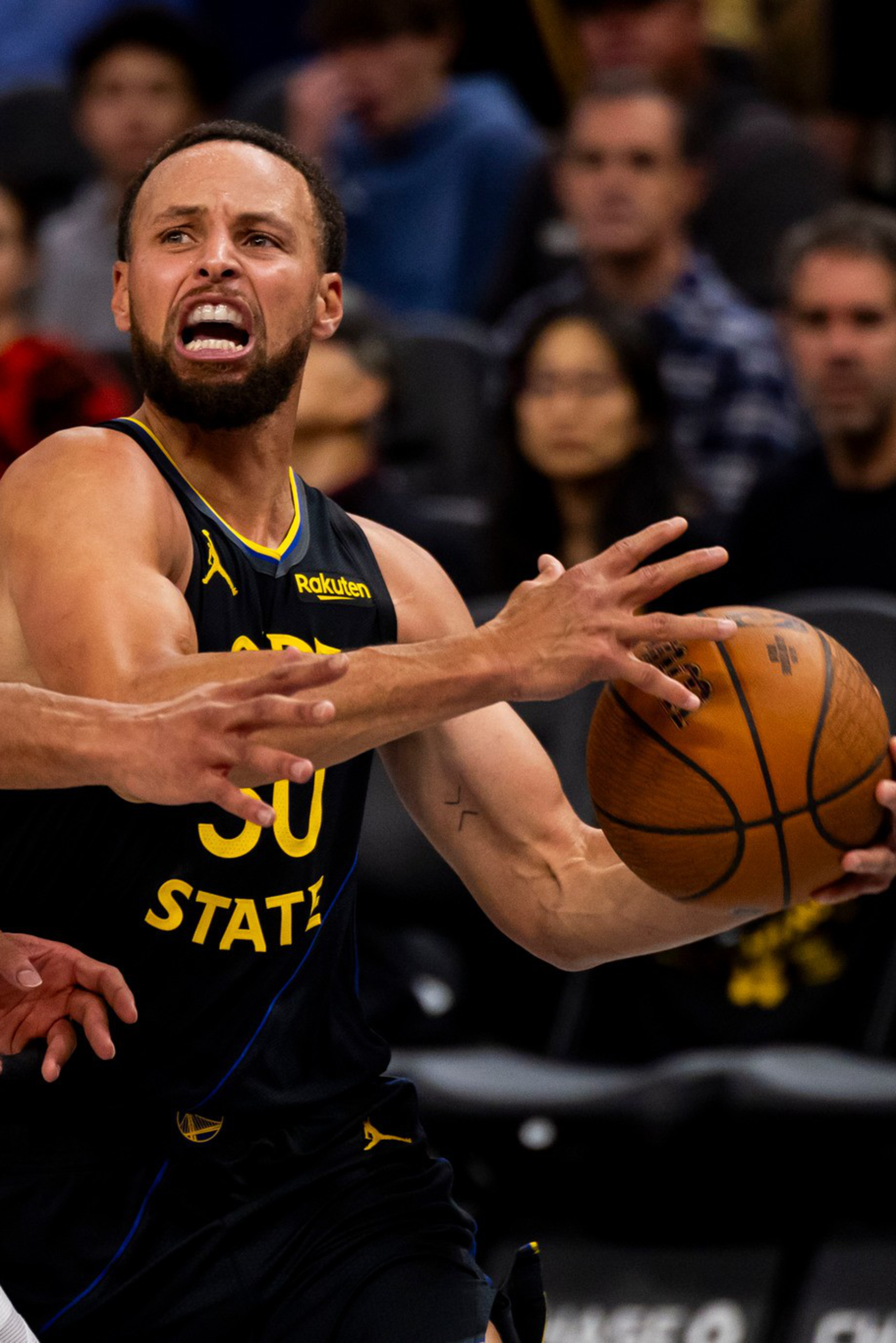 Stephen Curry, wearing a Golden State Warriors jersey, tightly grips a basketball while being closely defended by a player in a white Portland Trail Blazers uniform.
