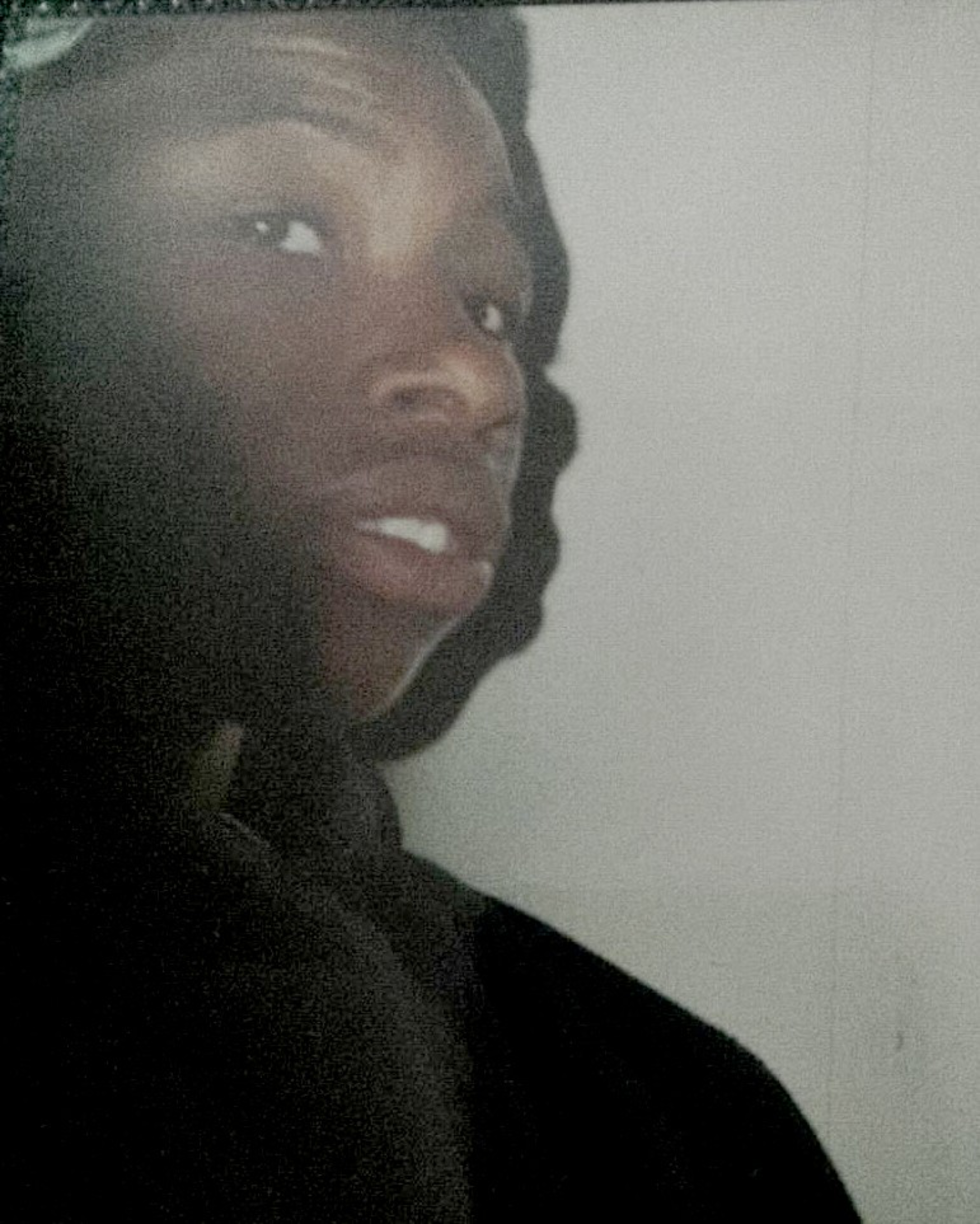 A person with dark skin looks slightly upward and to the left, set against a plain light background, with only their head and part of their shoulders visible.