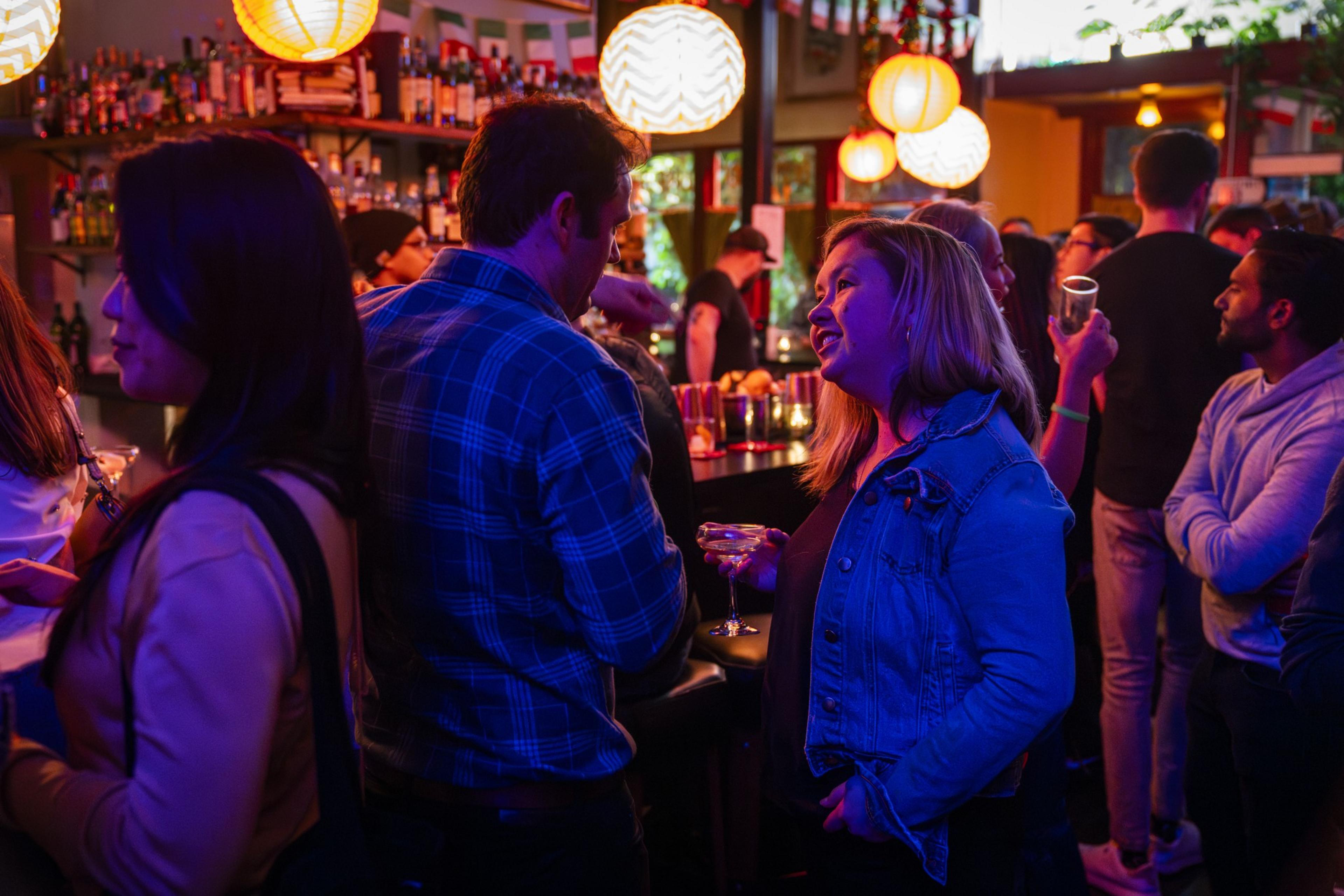 A woman holding a cocktail looks up at a man at a bar.