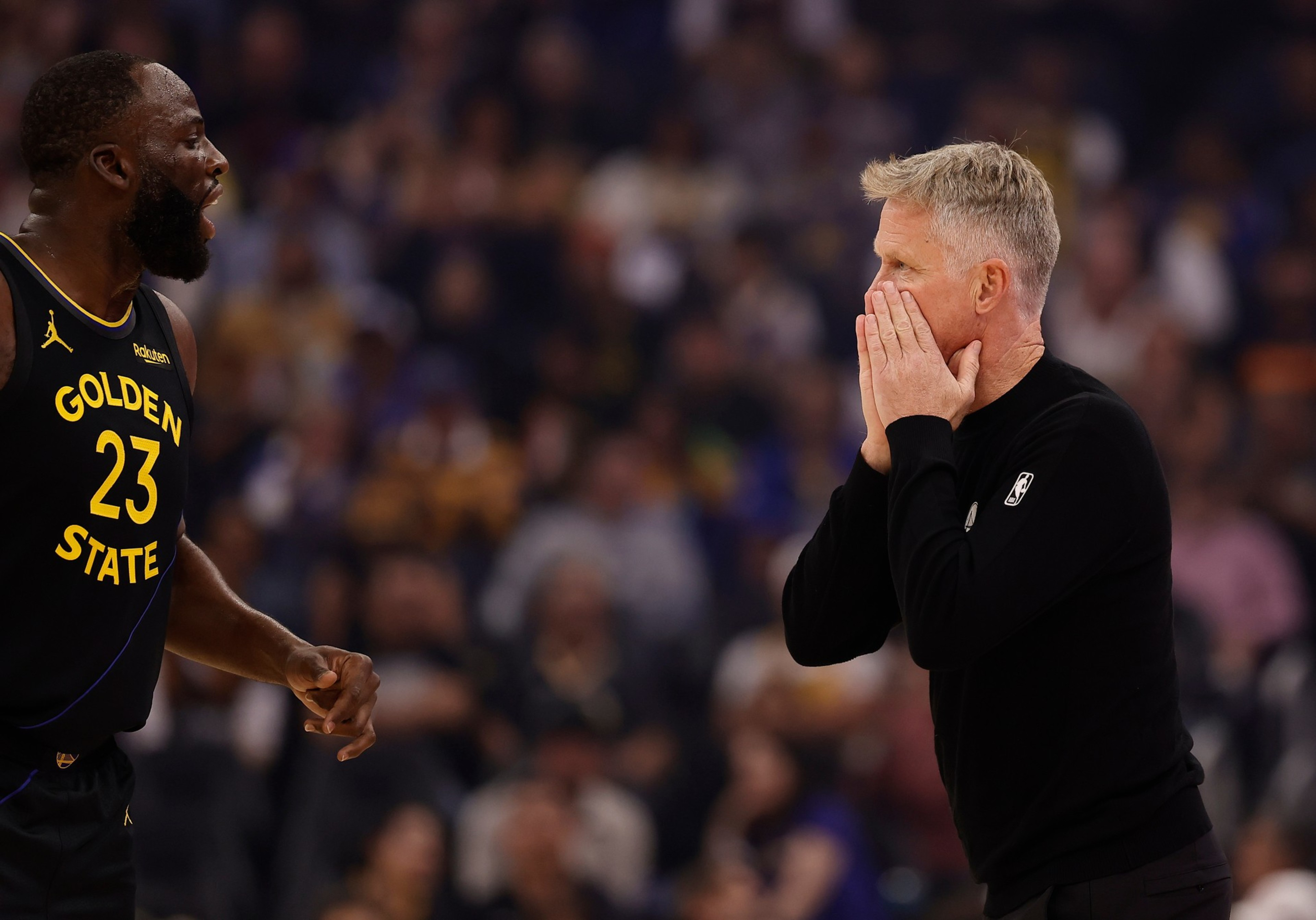 A Golden State Warriors player, wearing jersey number 23, is yelling while facing a coach who covers his mouth with his hands.