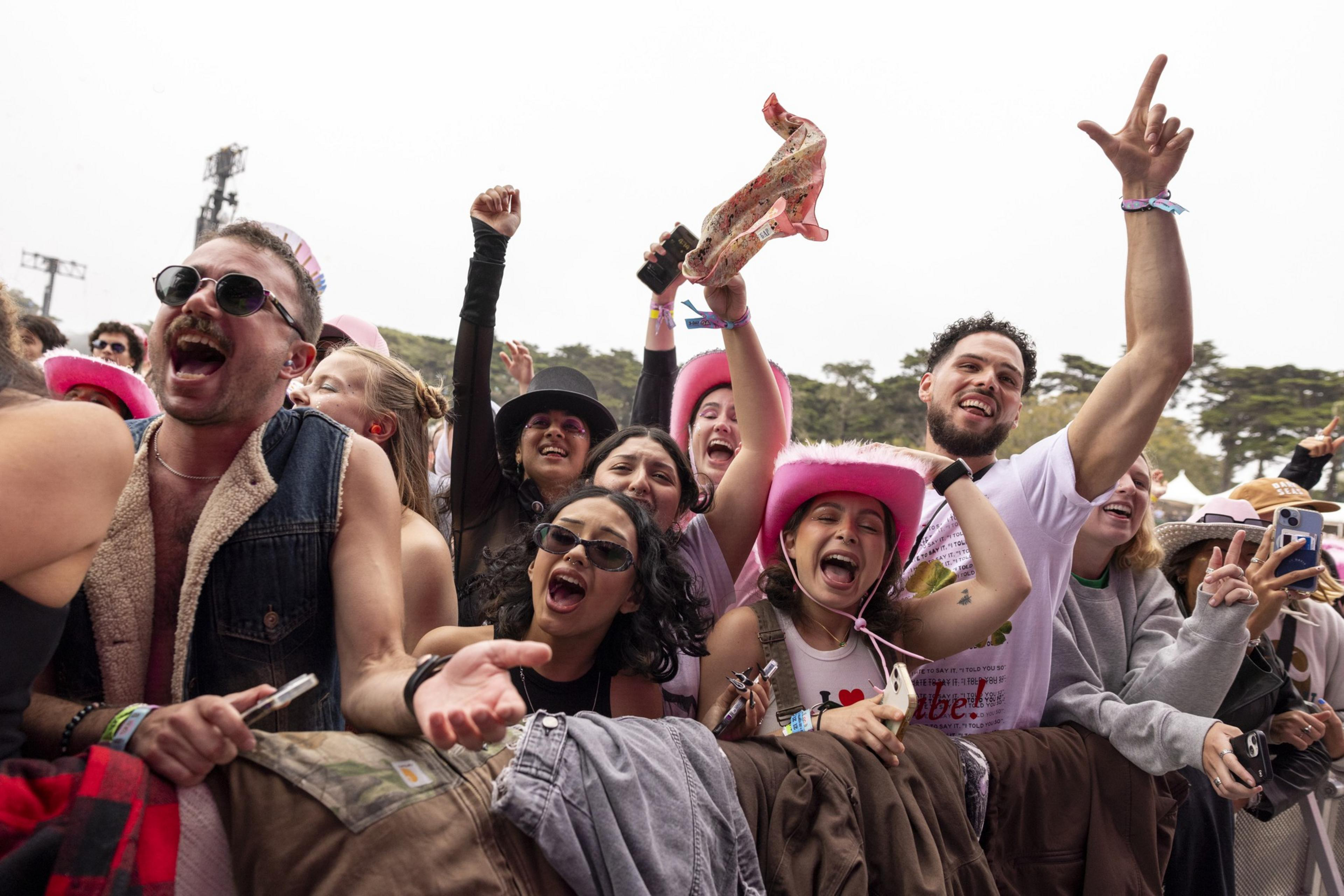A joyful group of people at a concert, some wearing pink cowboy hats, sunglasses, and excited expressions, cheering and raising their hands enthusiastically.