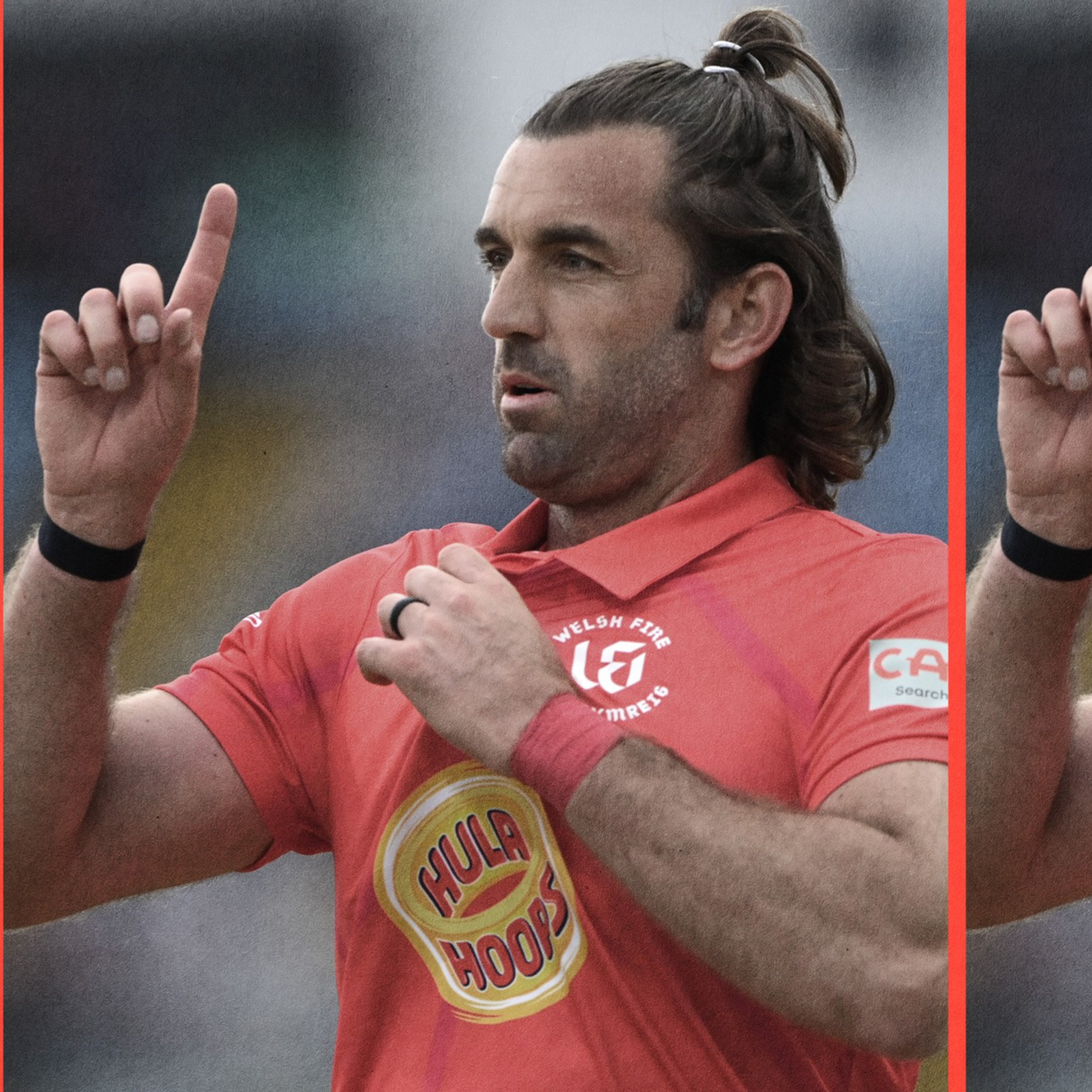 A man with long hair tied back wears a red sports jersey, raises both index fingers, and holds the shirt collar with one hand.