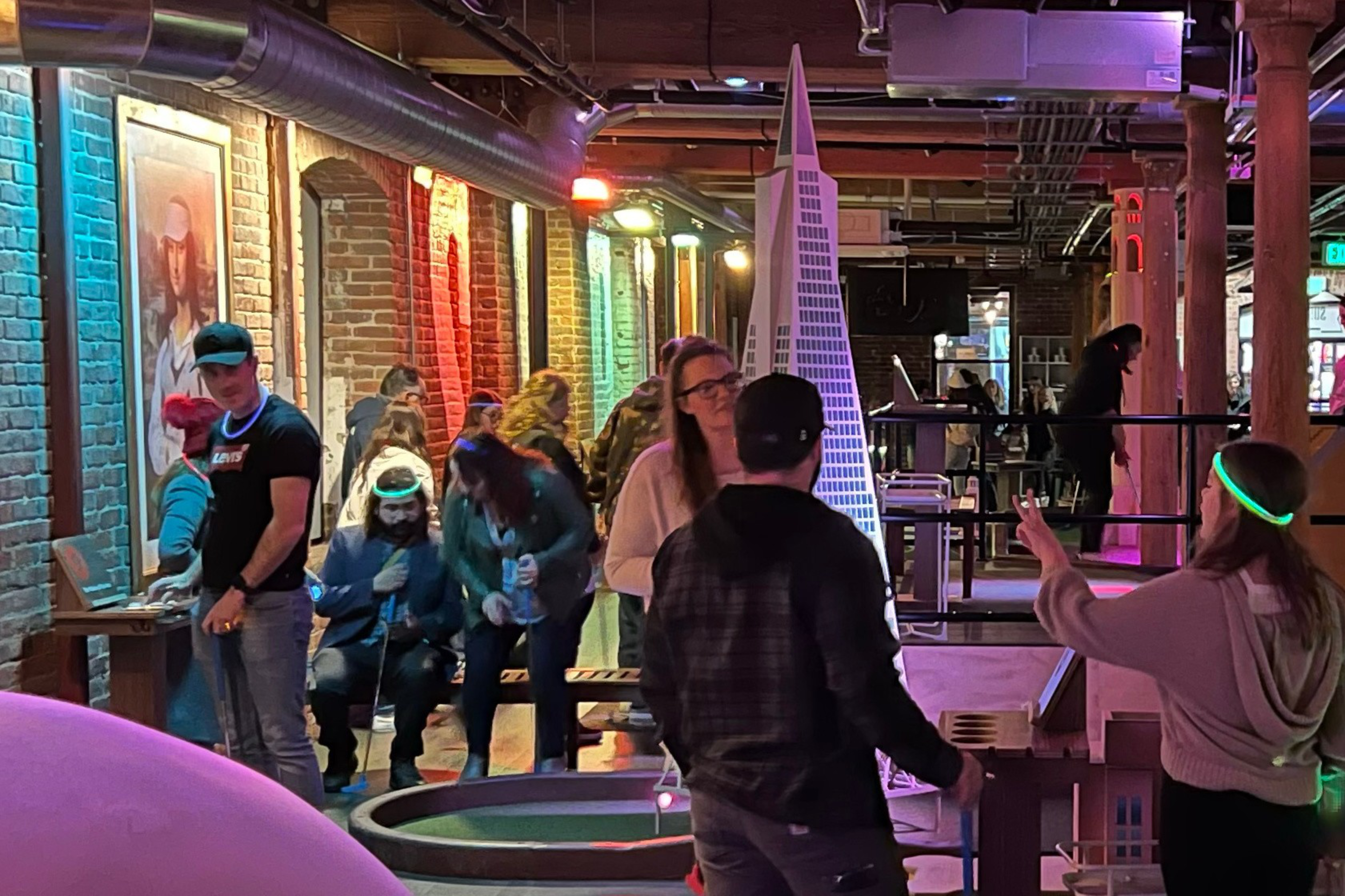 People mingle in an exposed-brick space next to a miniature model of the Transamerica Pyramid.