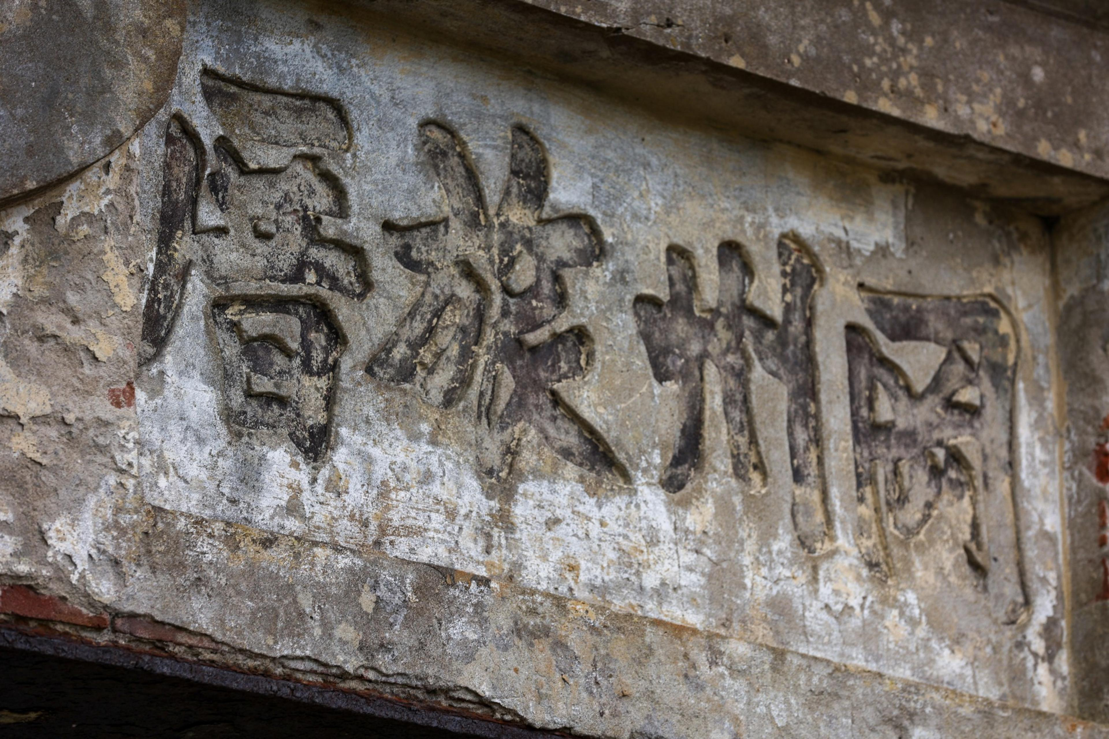 Four Chinese characters are carved into a weathered stone surface, showing signs of age and wear with faded gray and white patches.
