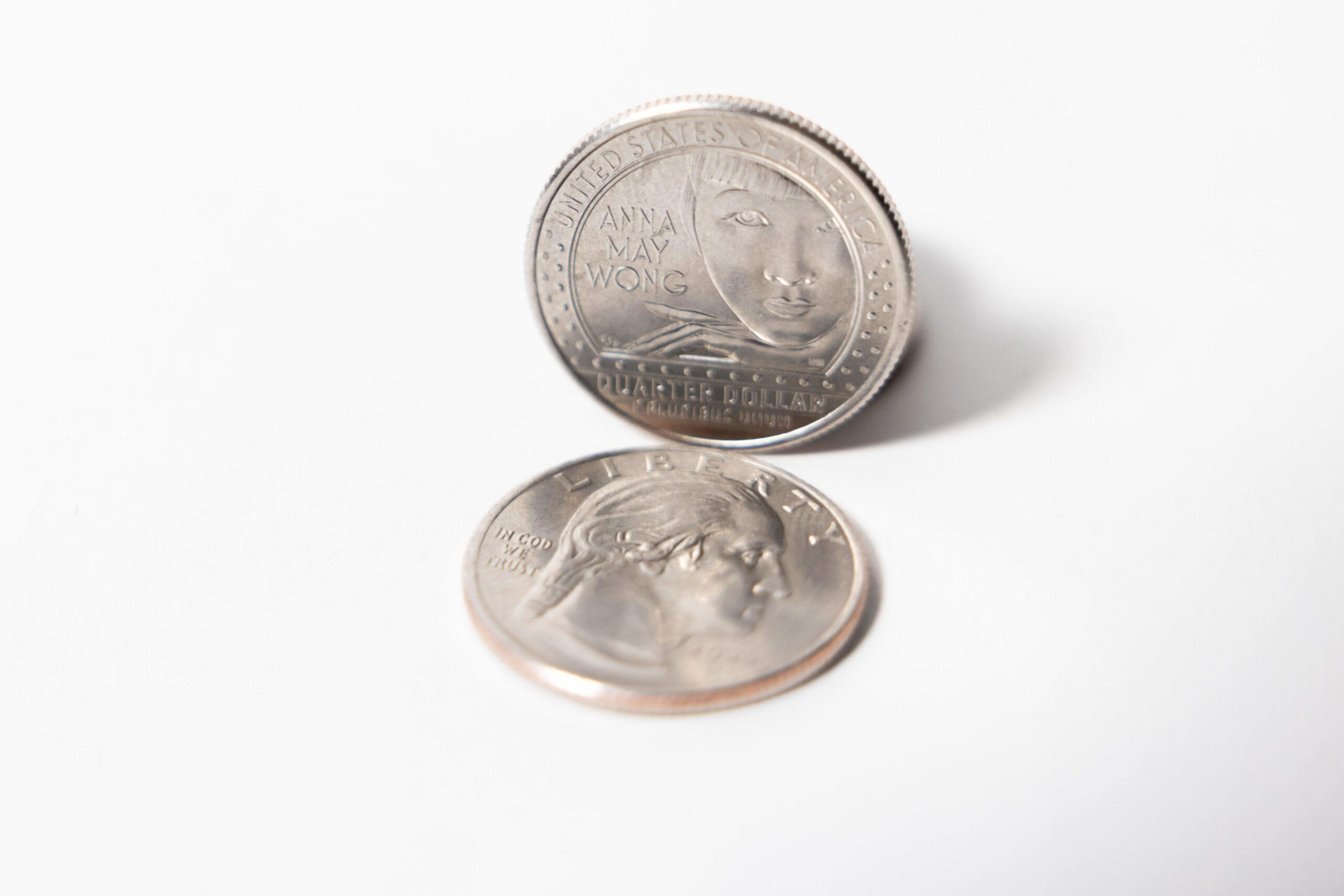 Two U.S. quarters are shown, one featuring Anna May Wong and the other showing George Washington’s profile with "LIBERTY" inscribed.