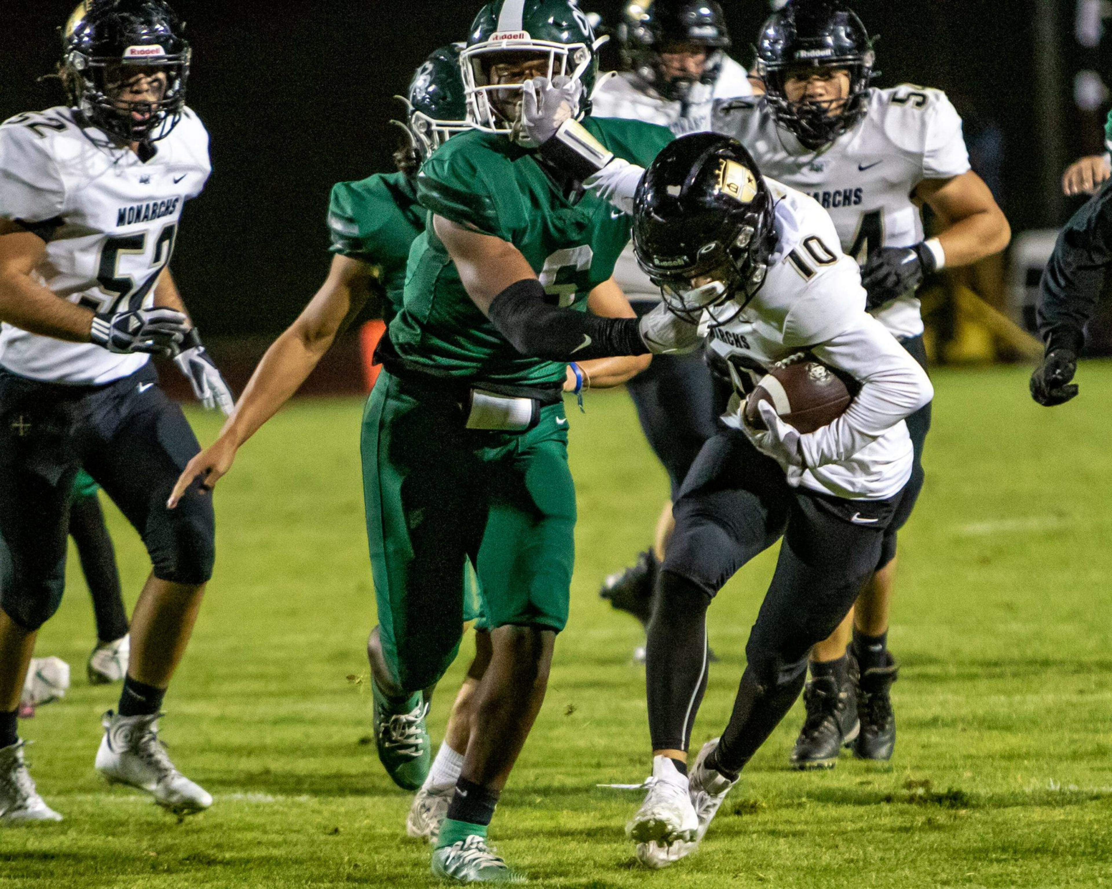 A football player in a white jersey runs with the ball while a player in a green jersey tries to block him during a night game.