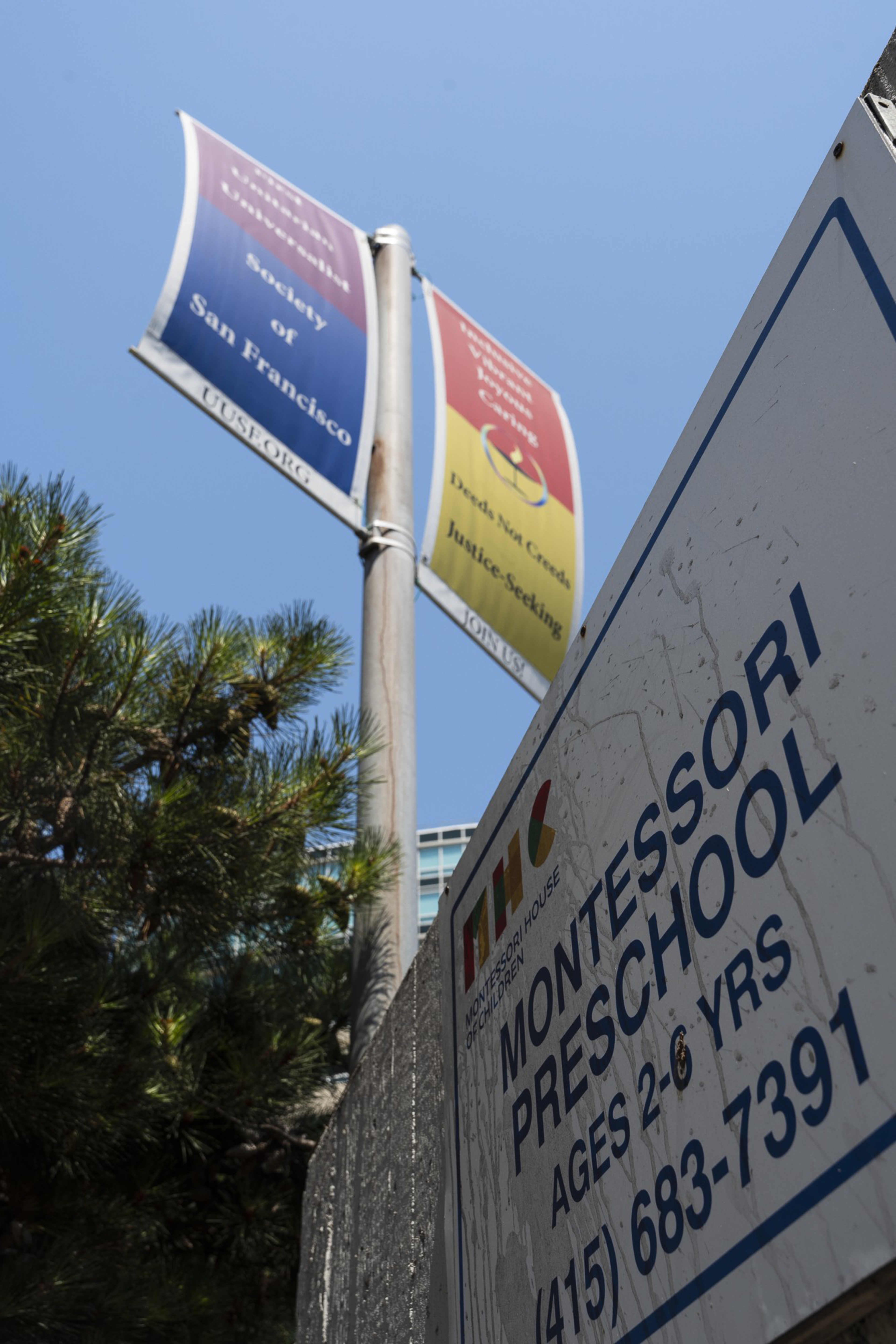 The image shows a sign for a Montessori preschool with contact information, set against a clear blue sky, with trees and banners in the background.
